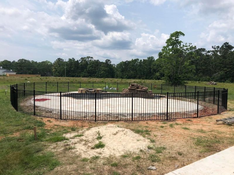 A black metal fence surrounds a swimming pool in a backyard.