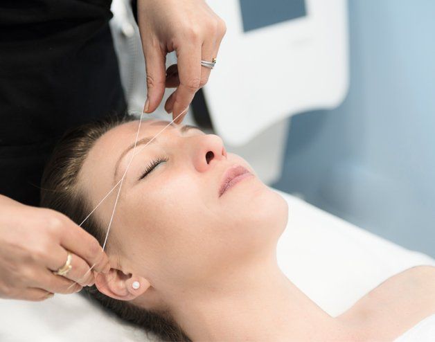 A woman is getting her eyebrows threaded in a beauty salon.
