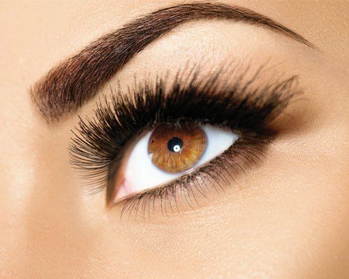 A close up of a woman 's eye with long eyelashes and well-shaped eyebrows.