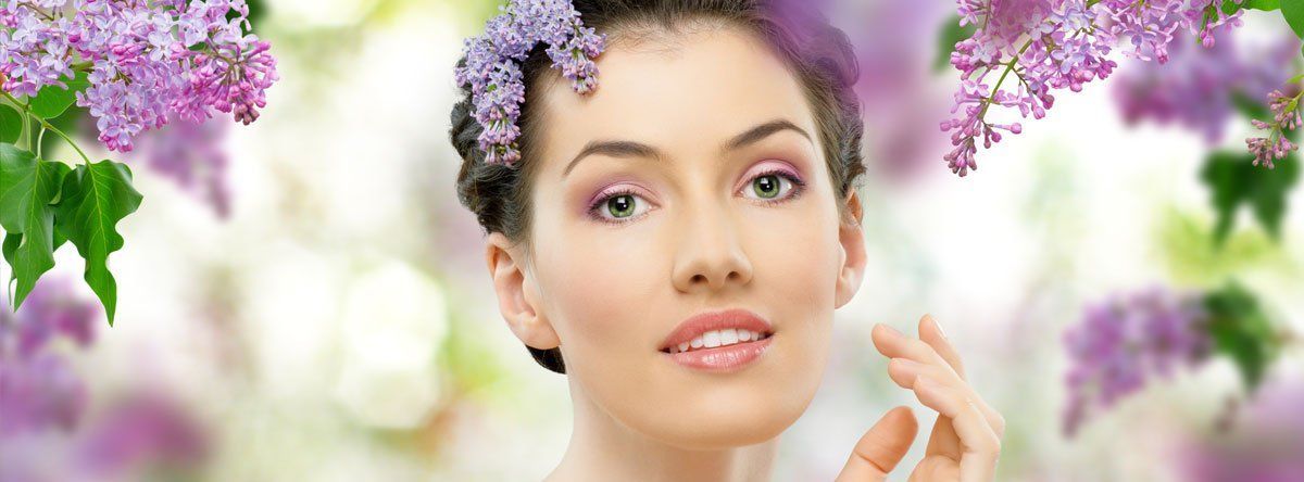 A woman with purple flowers in her hair is smiling.