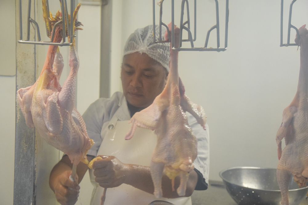 Un homme découpe des poulets dans une boucherie.
