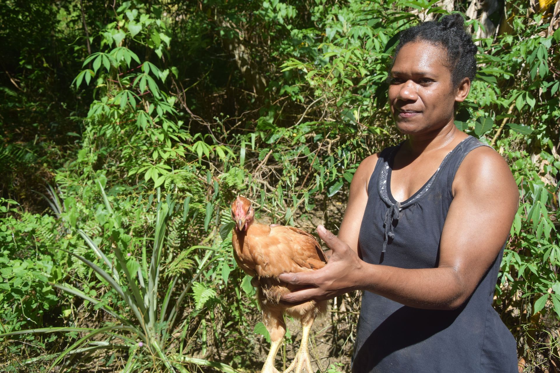 Une femme en débardeur noir tient un poulet dans ses mains.