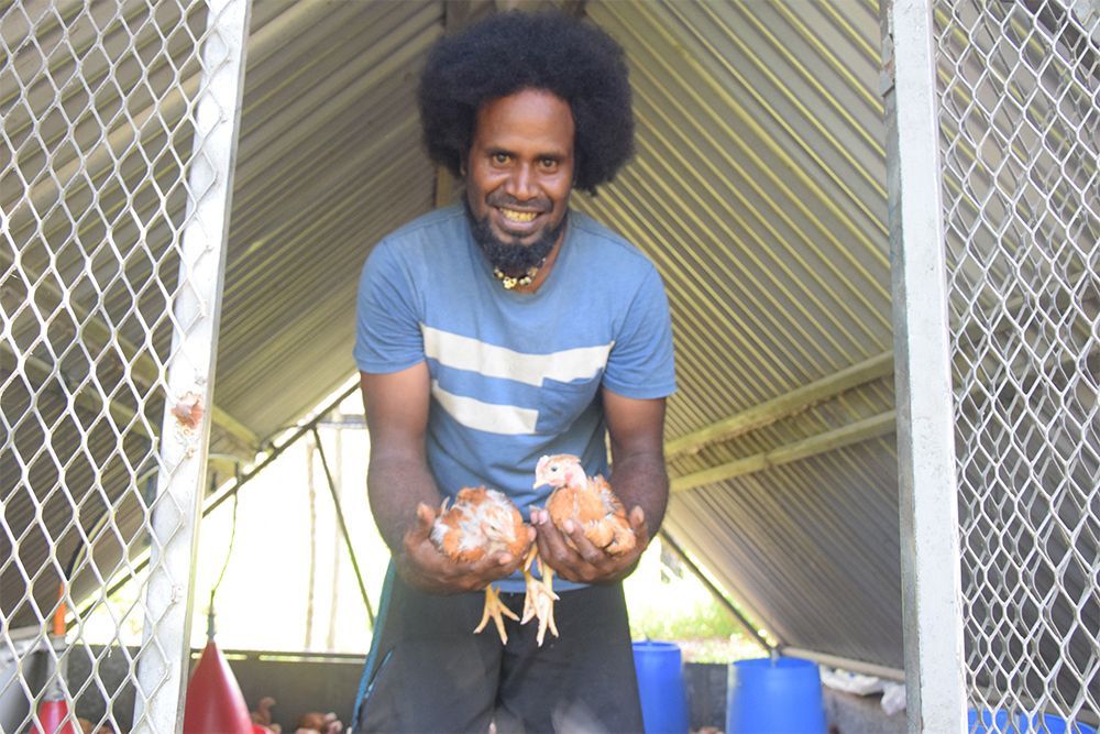 Un homme en chemise bleue tient deux poulets dans ses mains