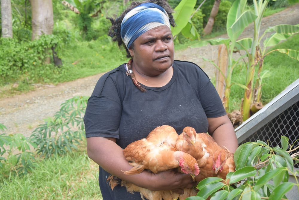 Une femme tient un poulet dans ses mains dans un champ.