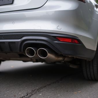 Rear view of a silver car with dual exhaust pipes. Tail light is red. Set on pavement.