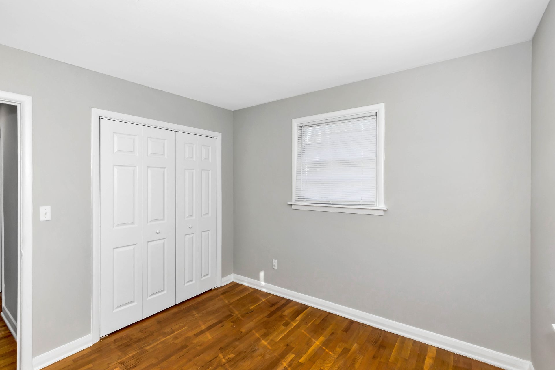 An empty bedroom with hardwood floors and a window.