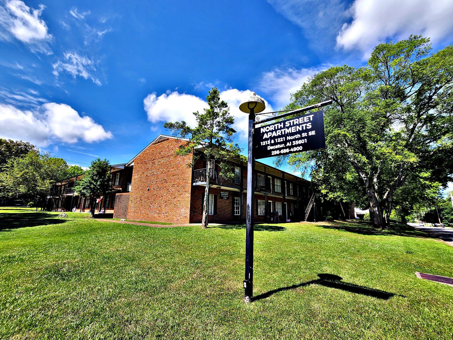 A sign is sitting in the grass in front of a brick building.