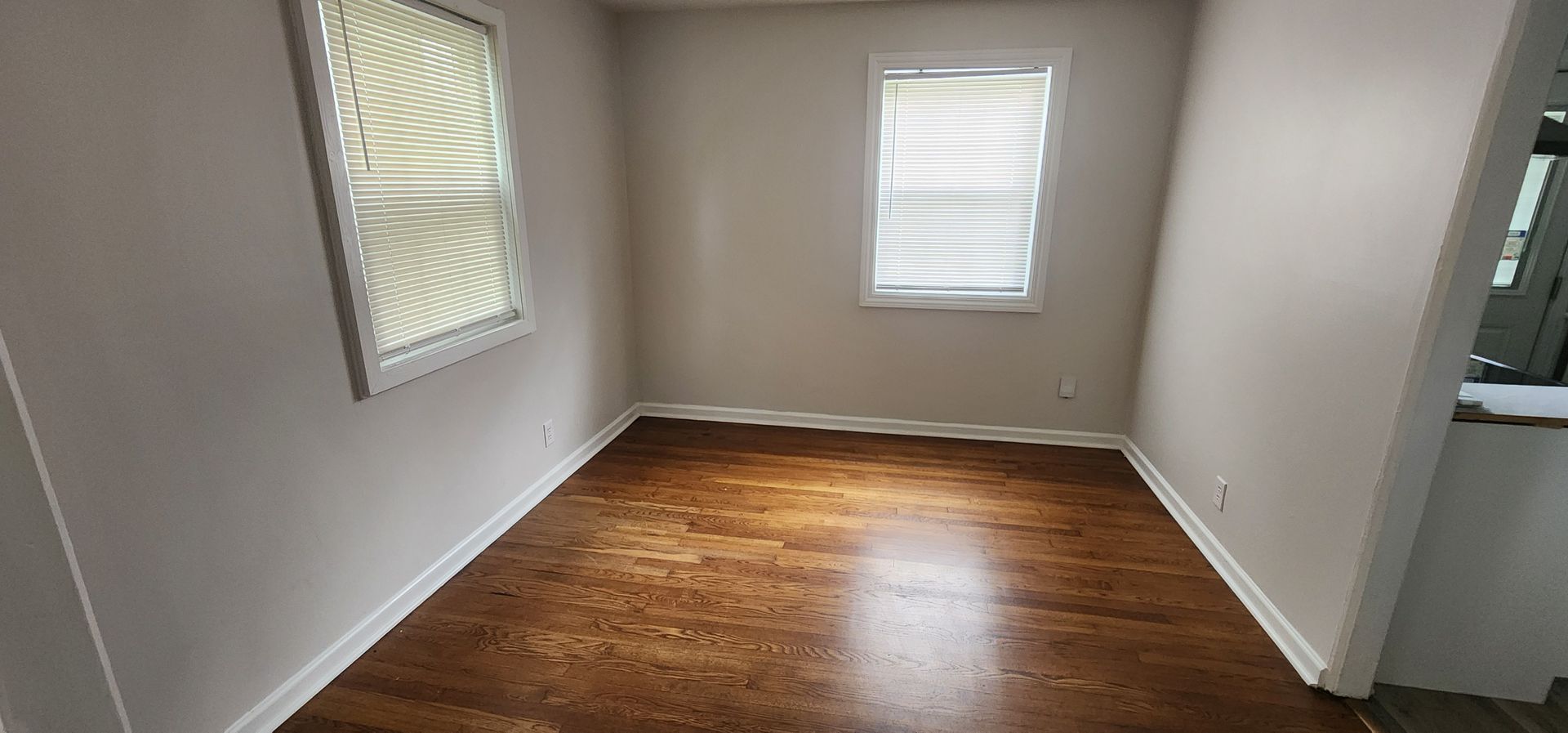 An empty room with hardwood floors and two windows.