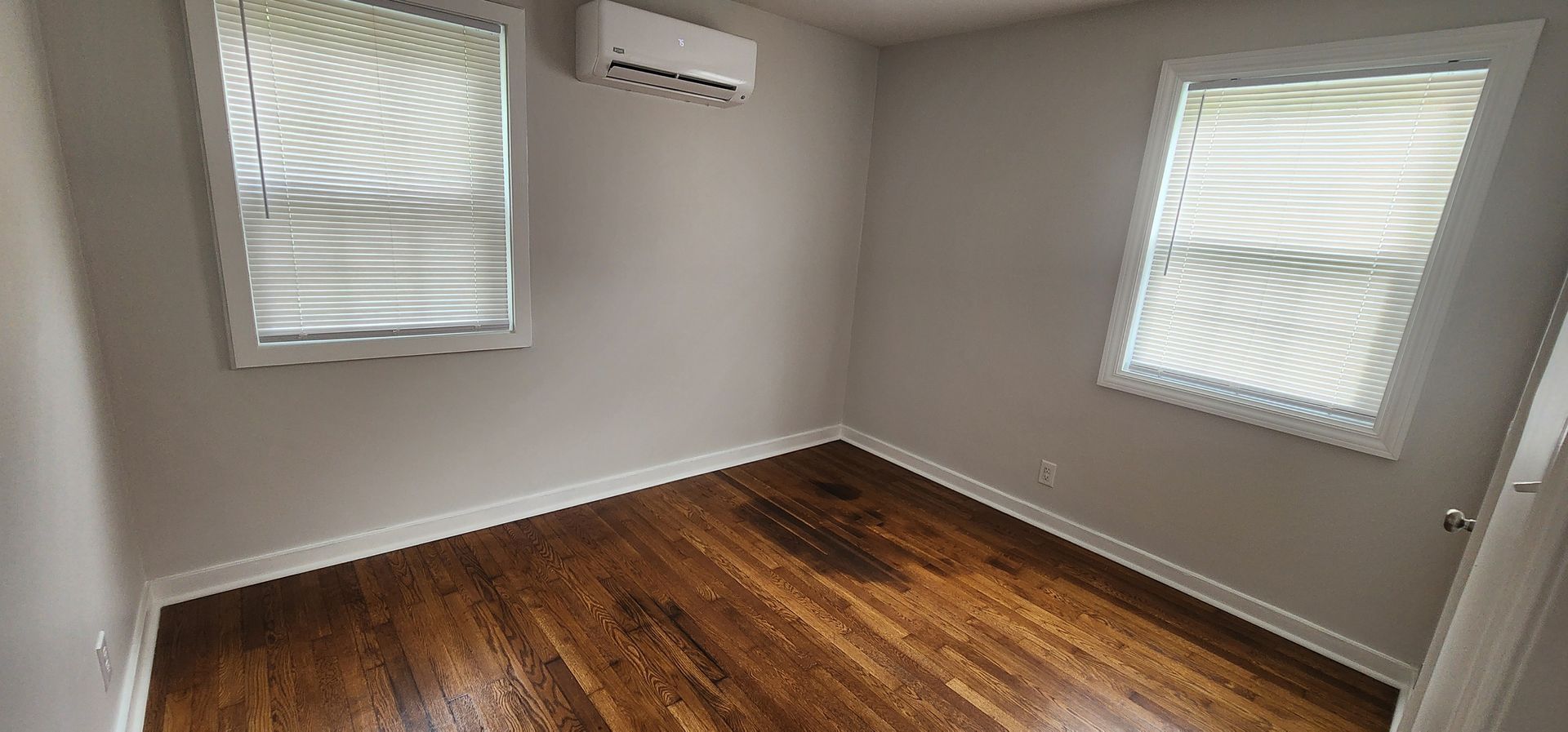 An empty room with hardwood floors and two windows.