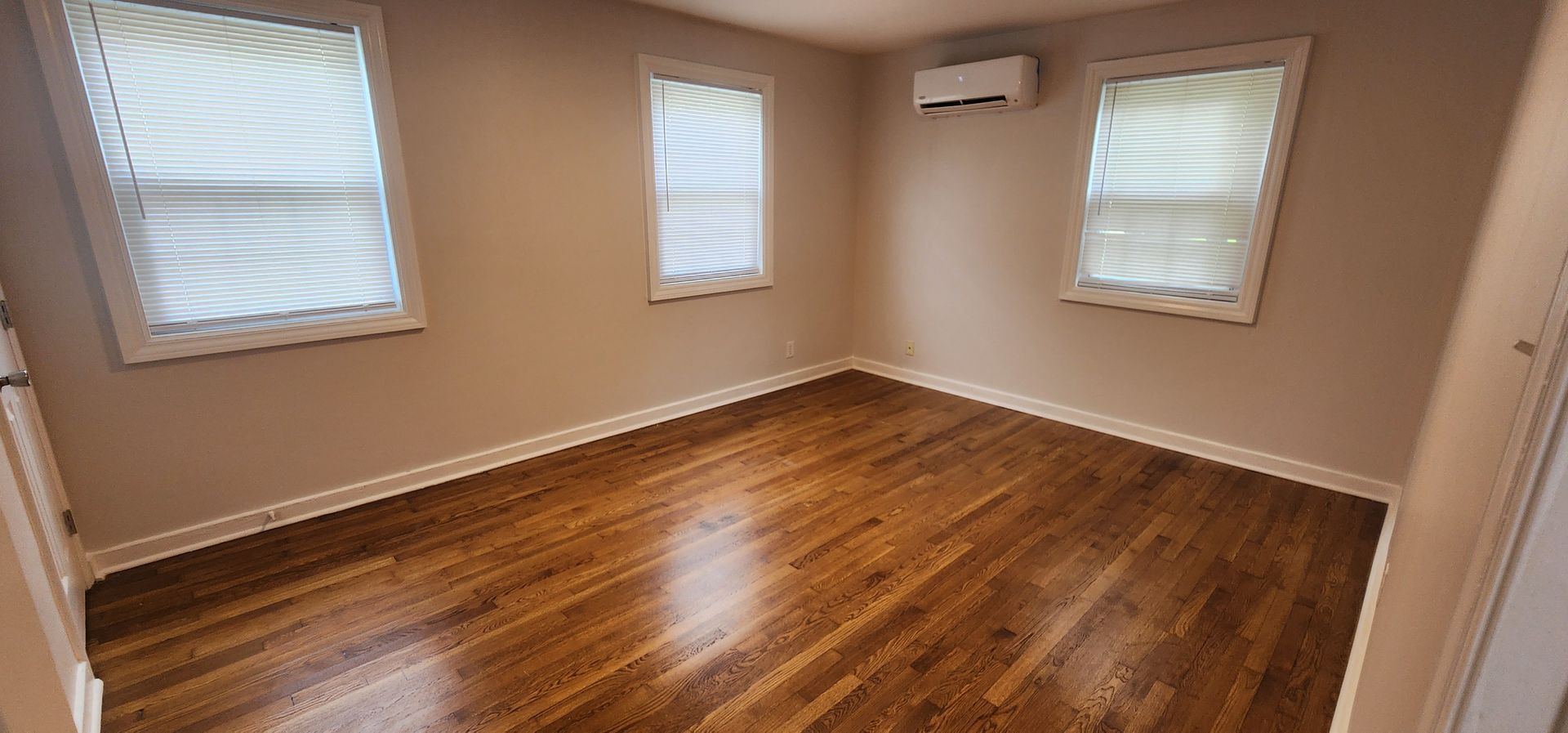 An empty room with hardwood floors and three windows.