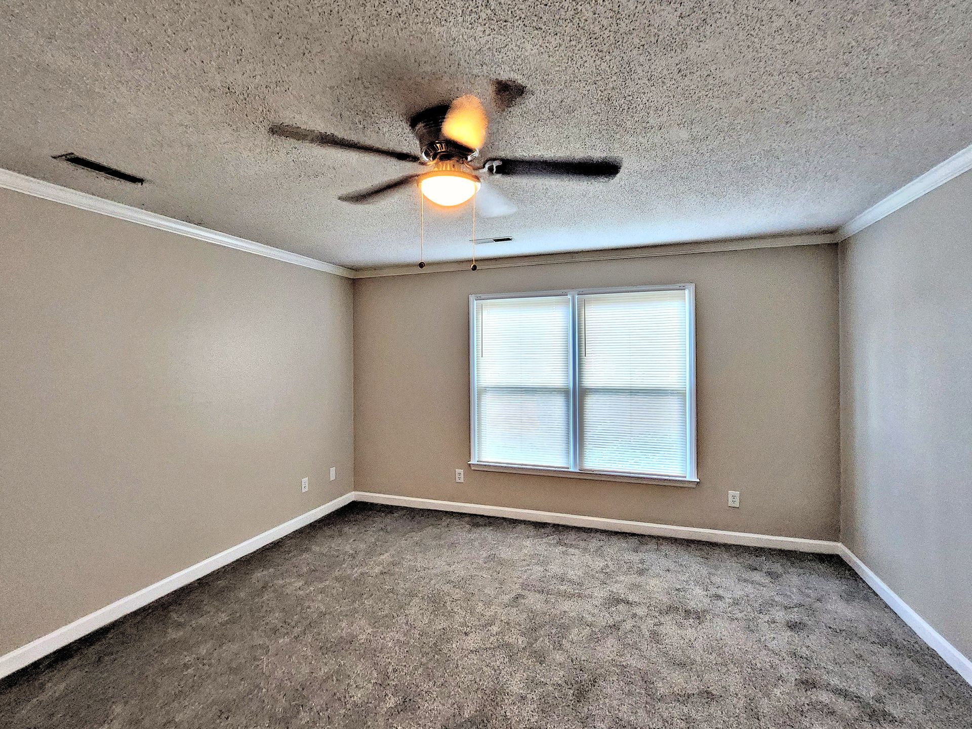 An empty living room with a ceiling fan and a window.