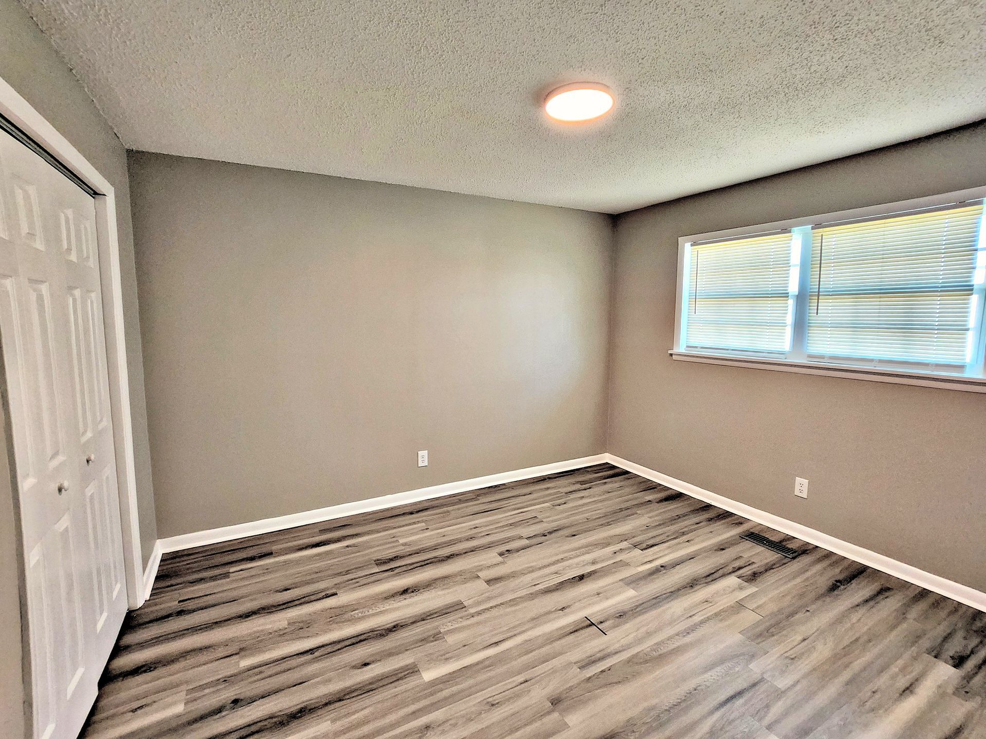 An empty bedroom with hardwood floors and two windows.
