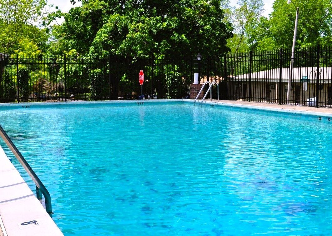 A large swimming pool surrounded by trees and a fence