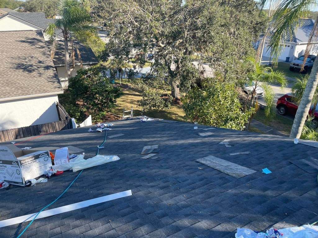 A roof is being repaired in a residential area with trees in the background.