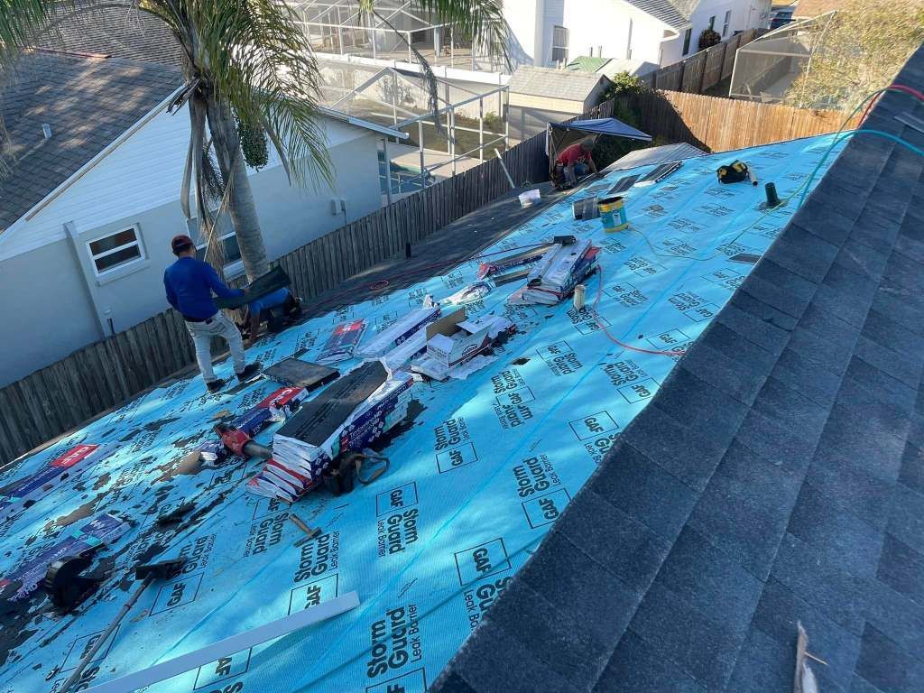 A man is standing on top of a roof with a blue tarp on it.