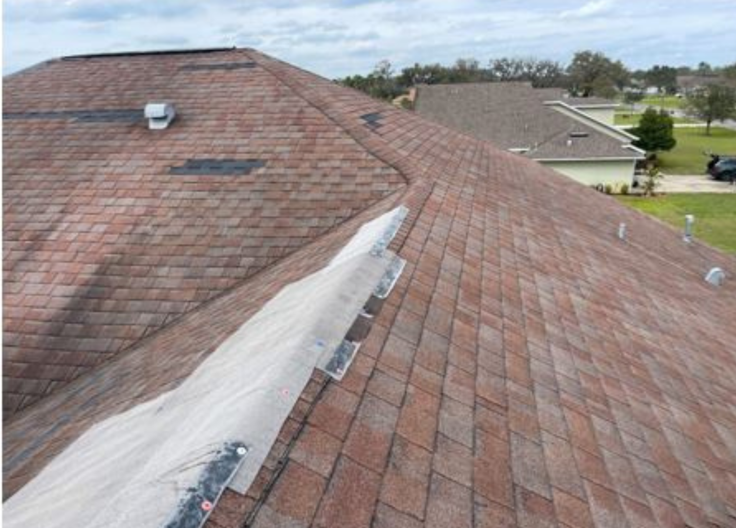 A close up of a roof with shingles on it and a house in the background.