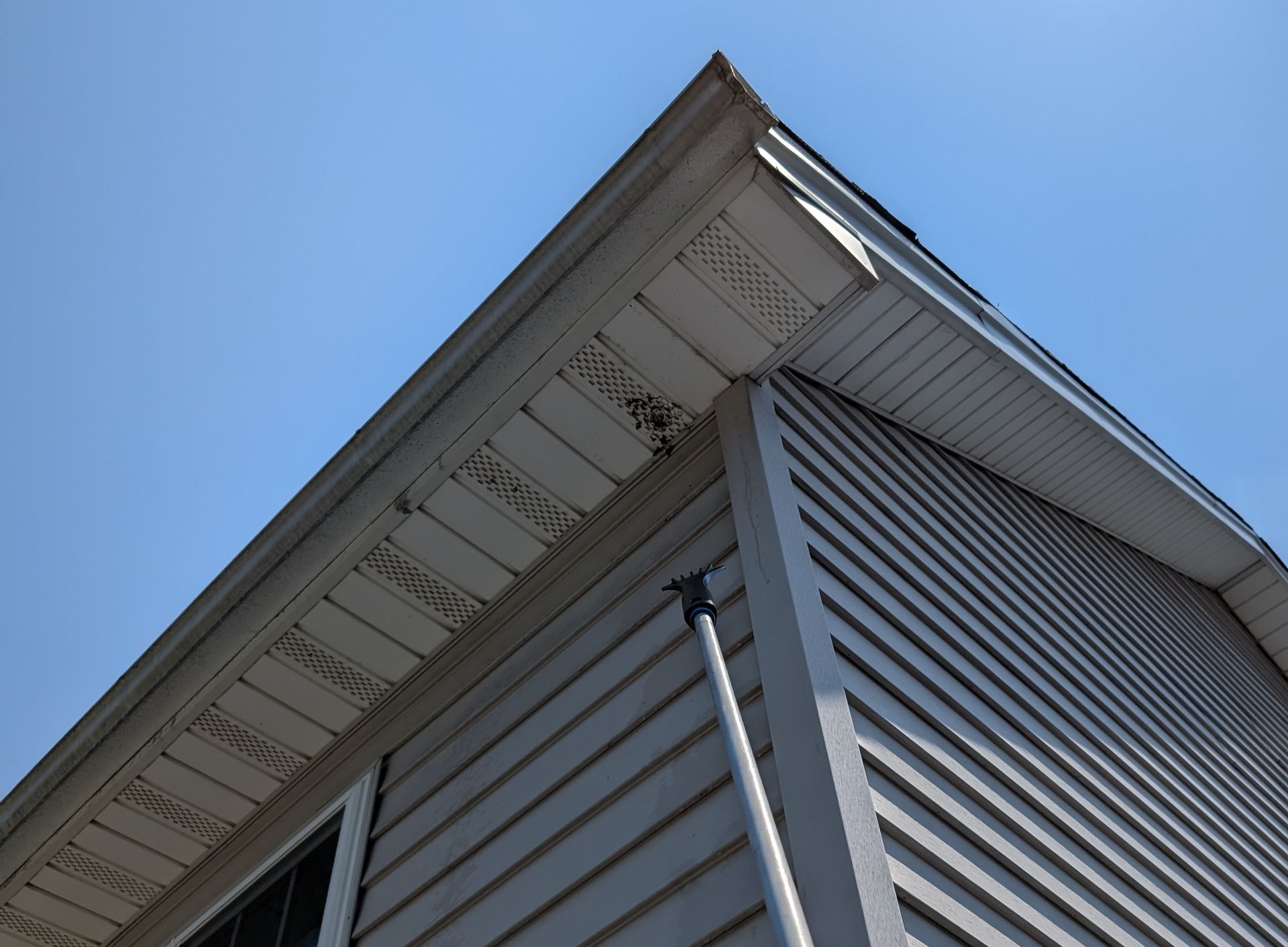 Corner of a house with gray siding and white soffit, against a blue sky.