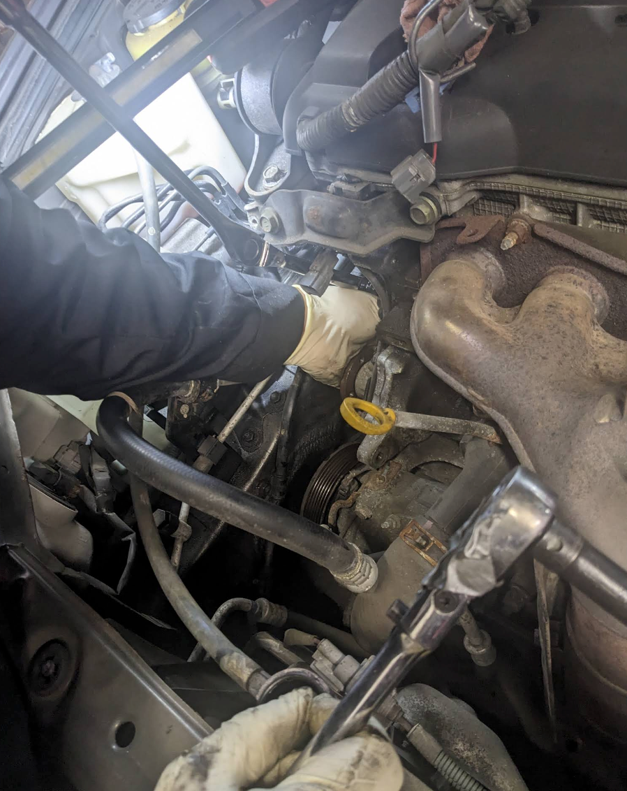Person wearing gloves works on a car engine, using a wrench and interacting with components. | Bovan’s Auto Services