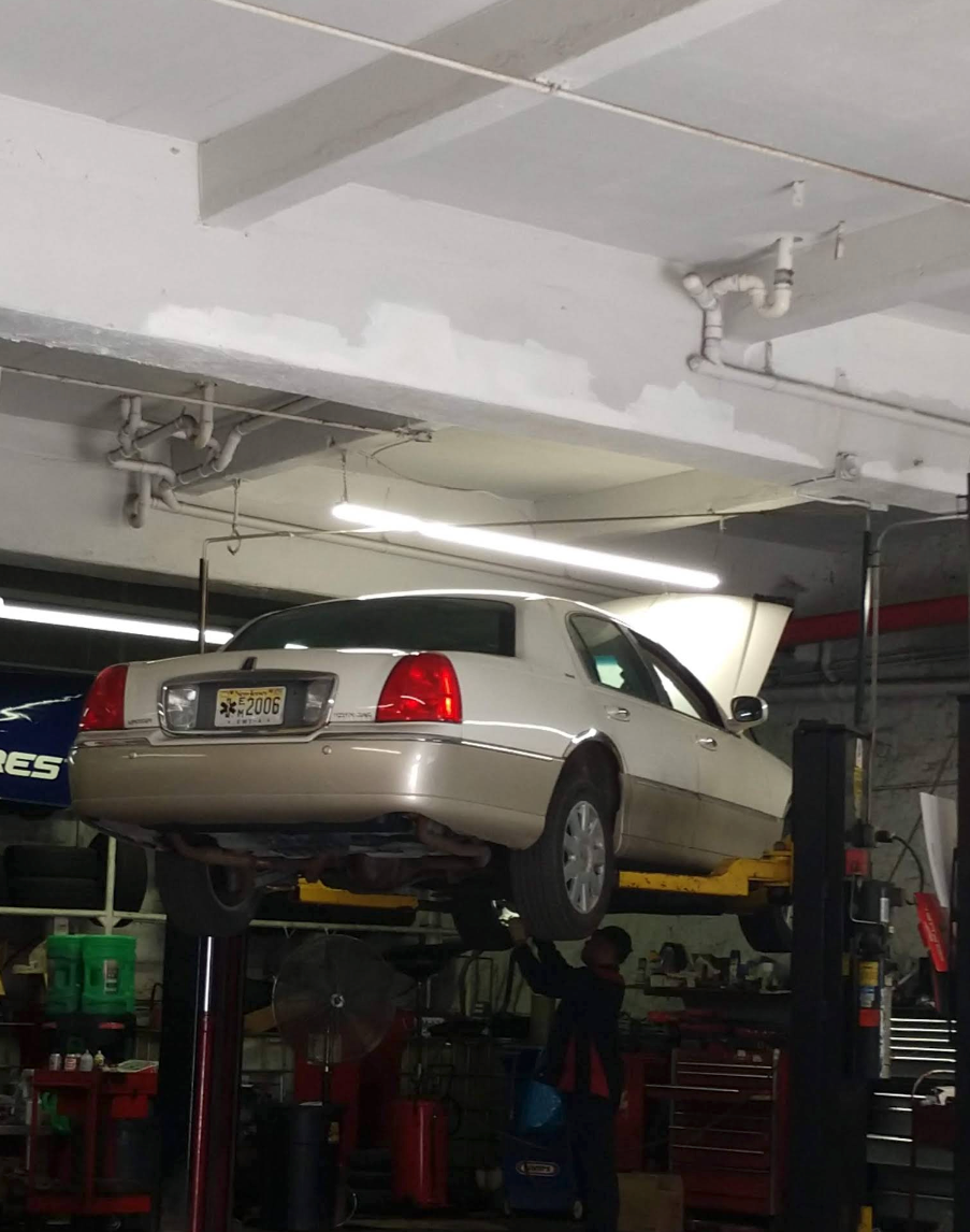 Car raised on a lift in a repair shop; mechanic working under the car. | Bovan’s Auto Services