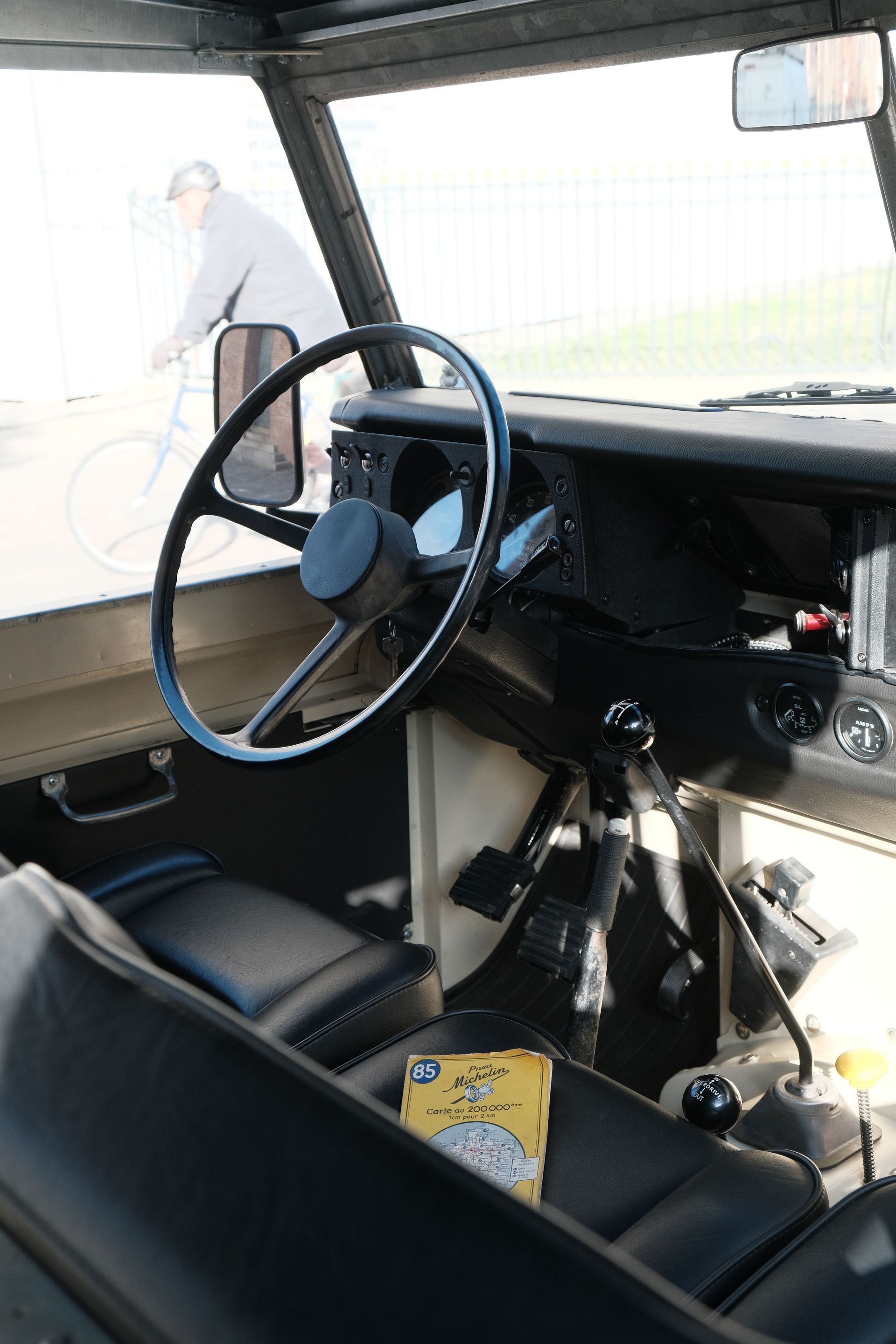 Intérieur d'un Land Rover noir vintage, avec une personne faisant du vélo à l'extérieur du pare-brise.