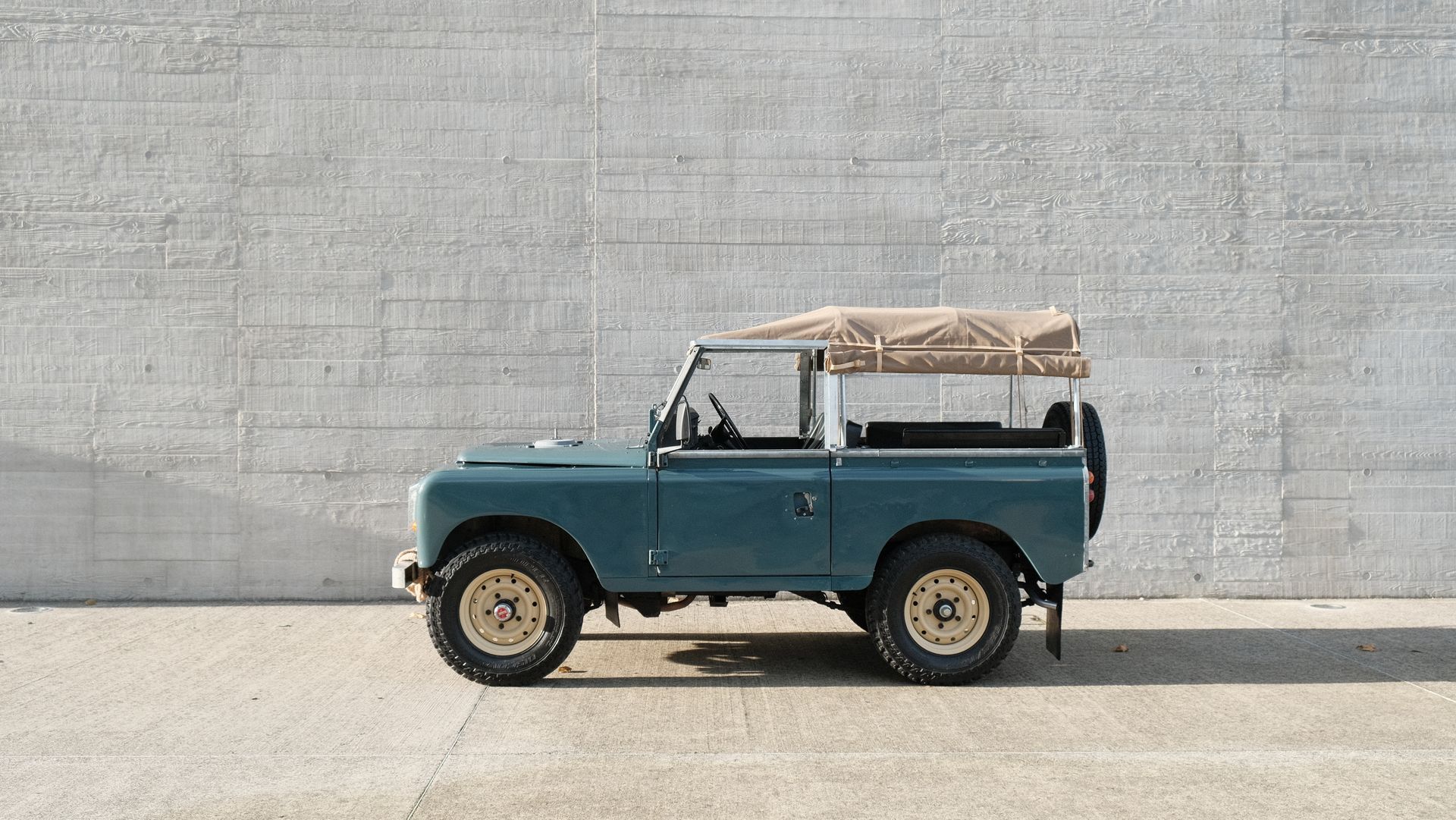 Land Rover vintage bleu avec toit beige garé devant un mur en béton.