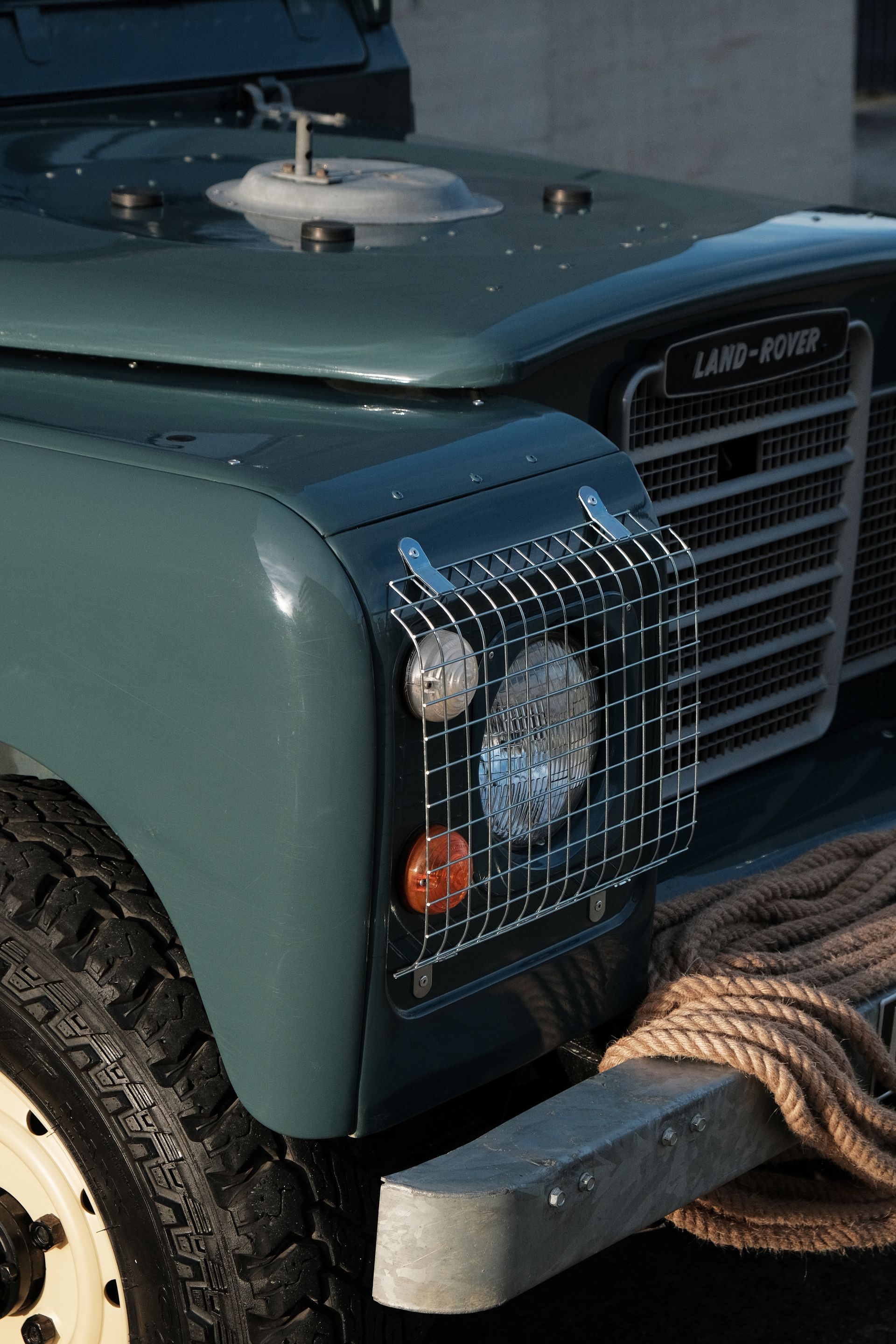 Land Rover Defender bleu sarcelle avec un protège-phare et une corde drapée sur le pare-chocs.