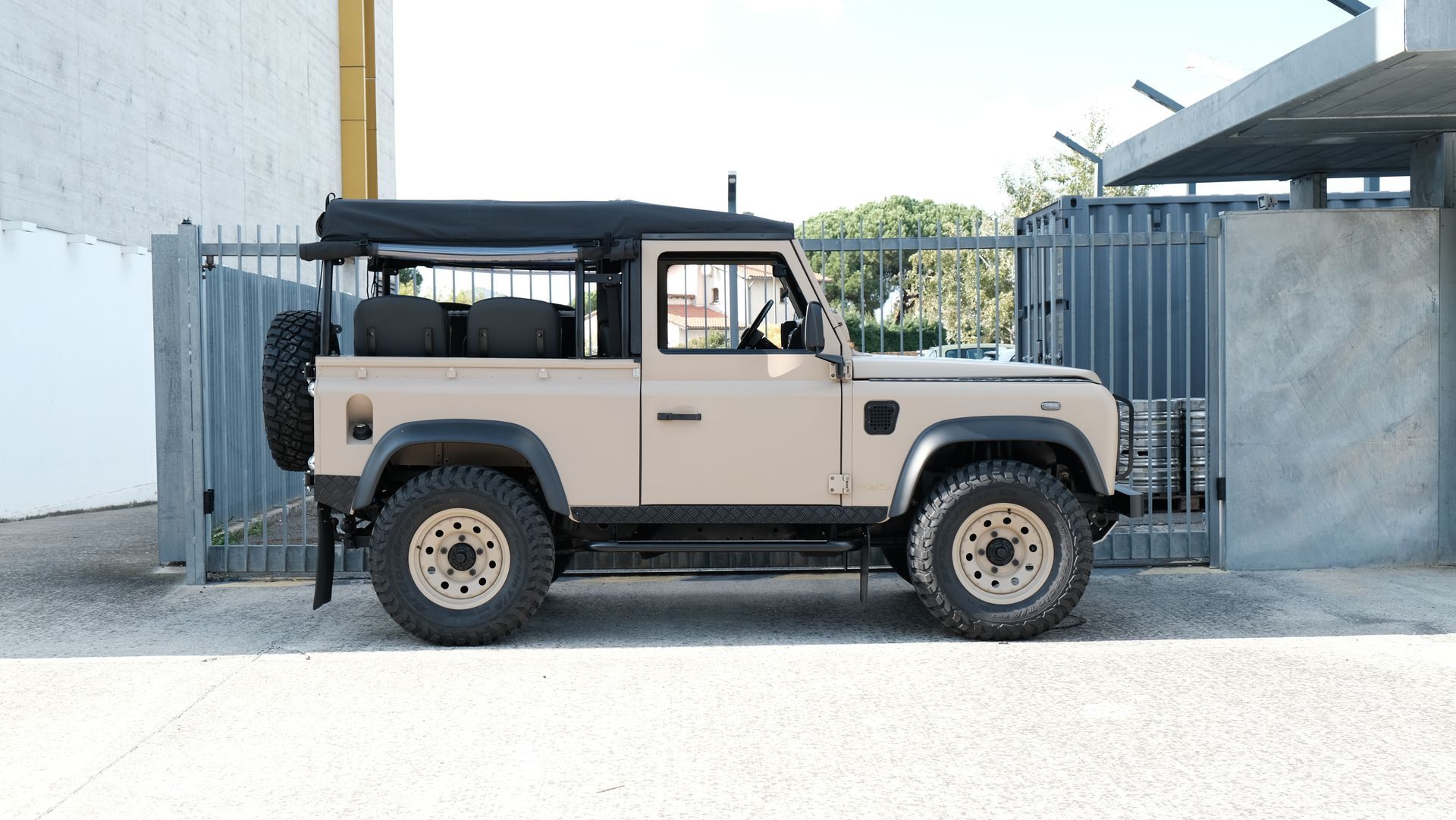 Land Rover Defender beige, toit noir, garée près d'un portail.