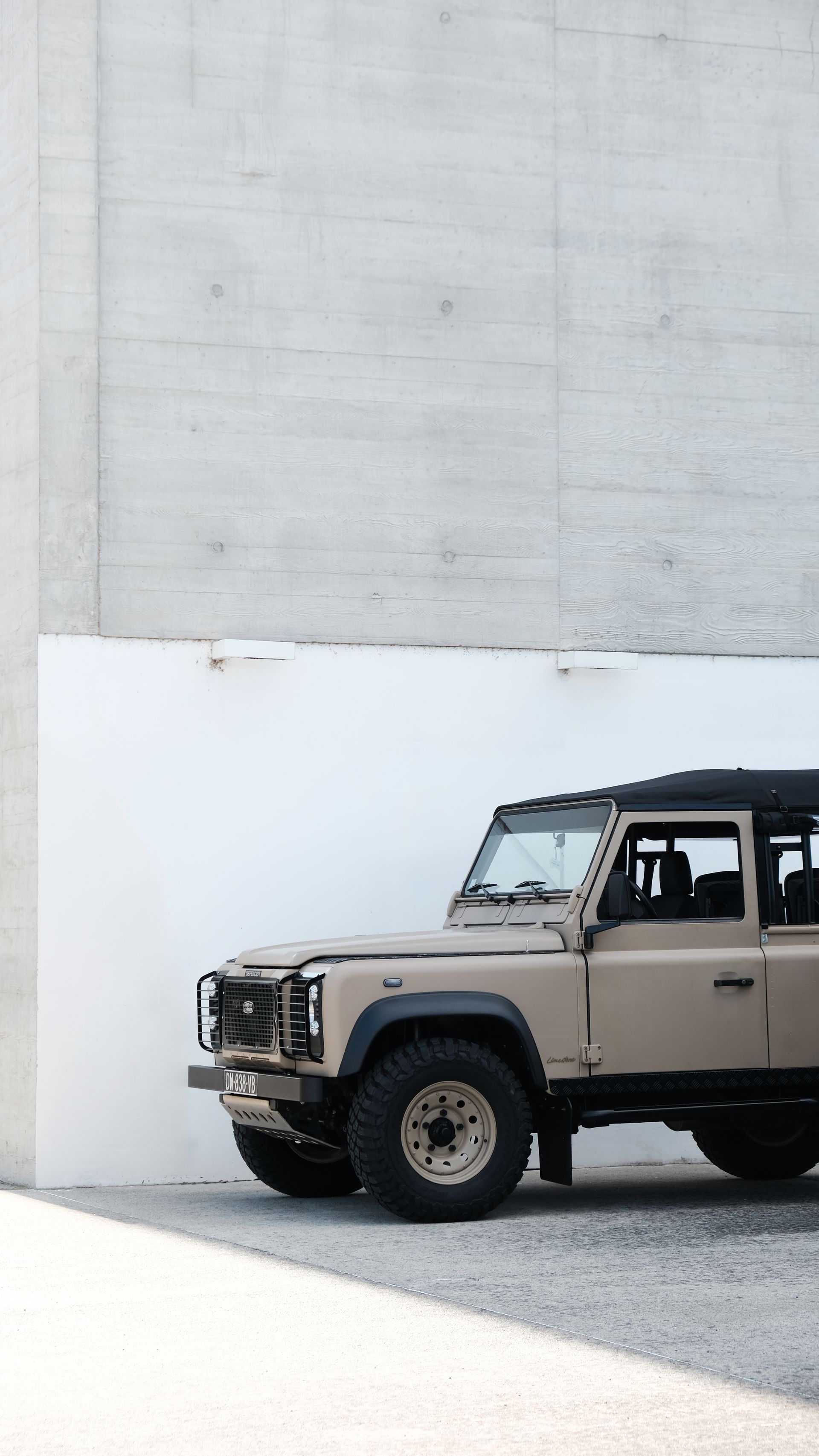 Land Rover beige garé à côté d'un mur de béton blanc et gris.