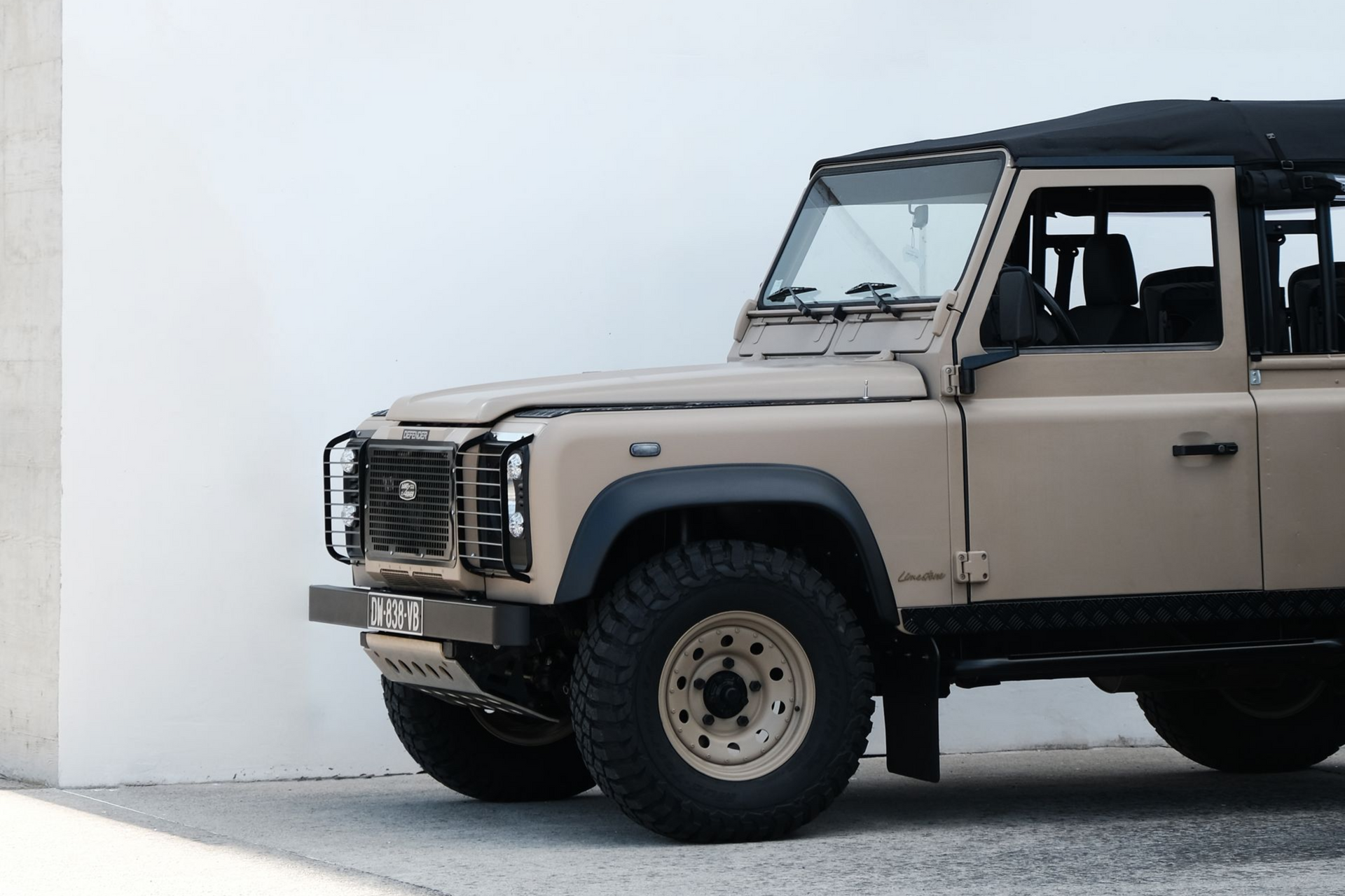 Land Rover Defender beige garée contre un mur blanc.