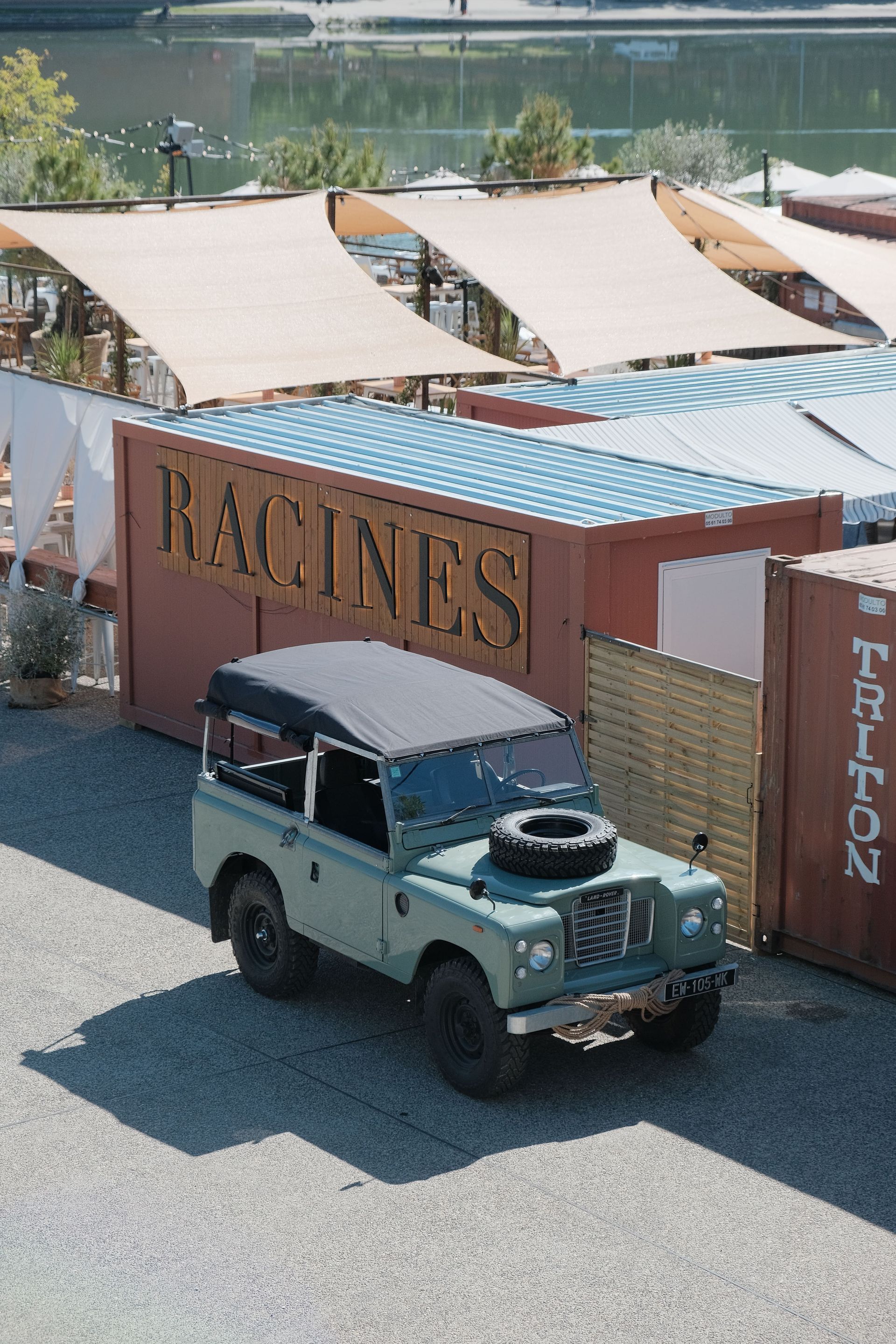 Land Rover vert garé devant un restaurant fait de conteneurs maritimes, près de l'eau.