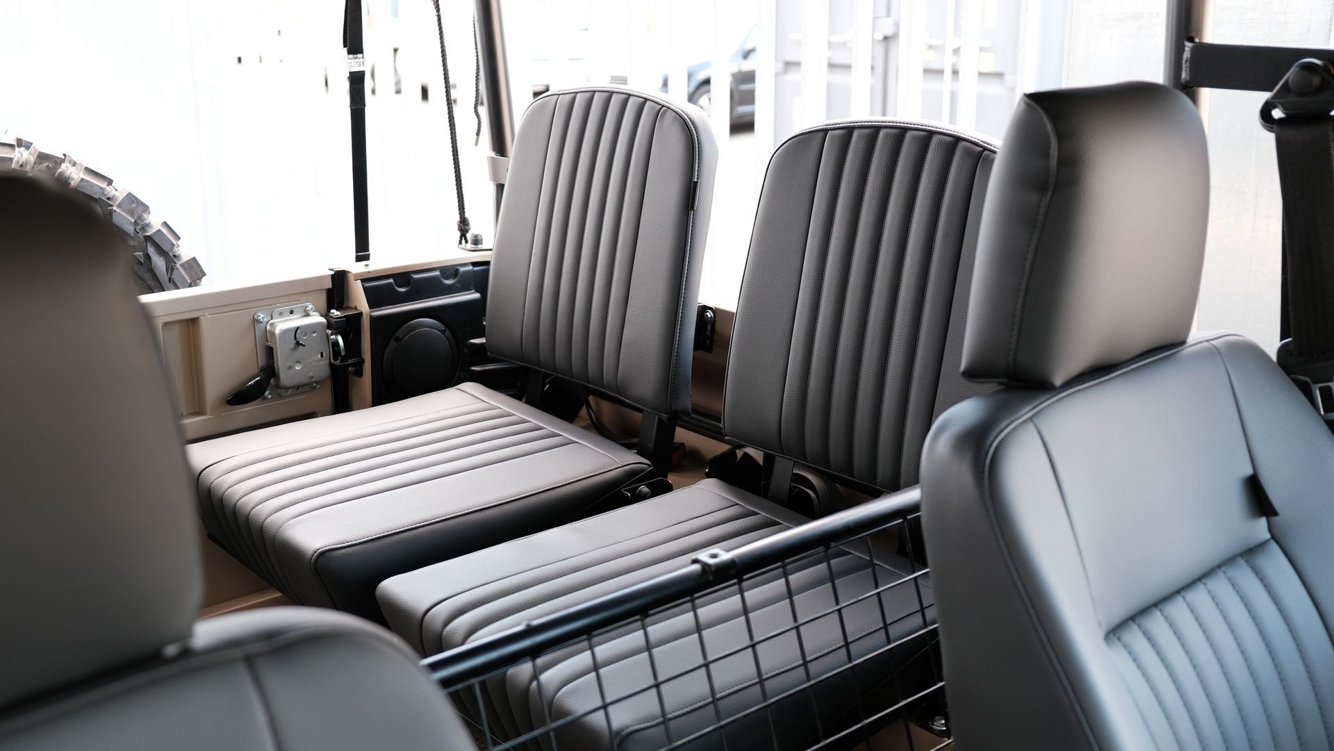 Intérieur d'un véhicule, montrant deux sièges passagers recouverts de tissu gris et une cage métallique noire.