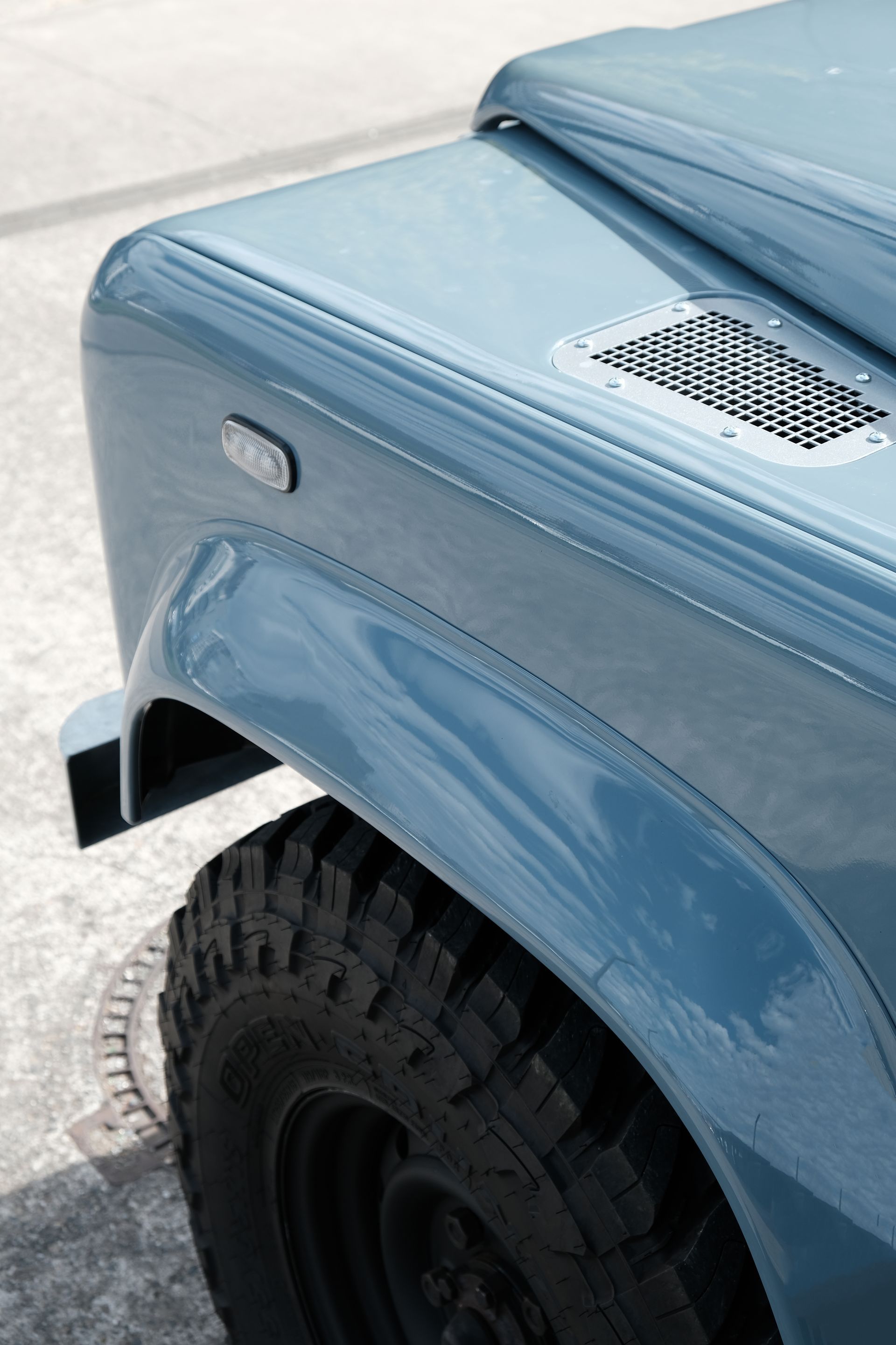 Panneau avant du Land Rover Defender bleu avec un pneu noir, une ventilation latérale et un capot surélevé.