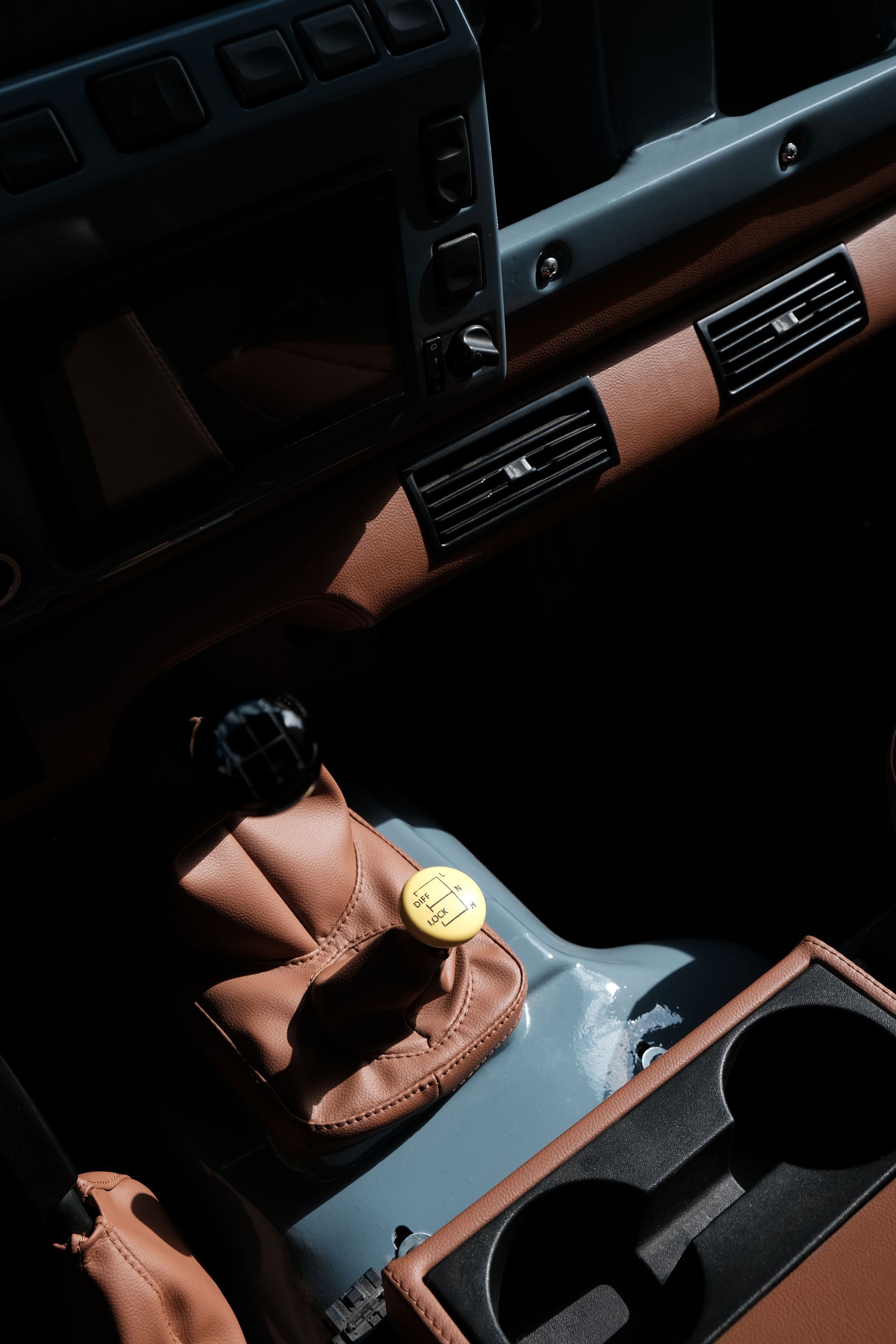 Vue intérieure du tableau de bord et de la console d'une voiture. Détails en cuir marron, garnitures grises et pommeau de levier de vitesse jaune.