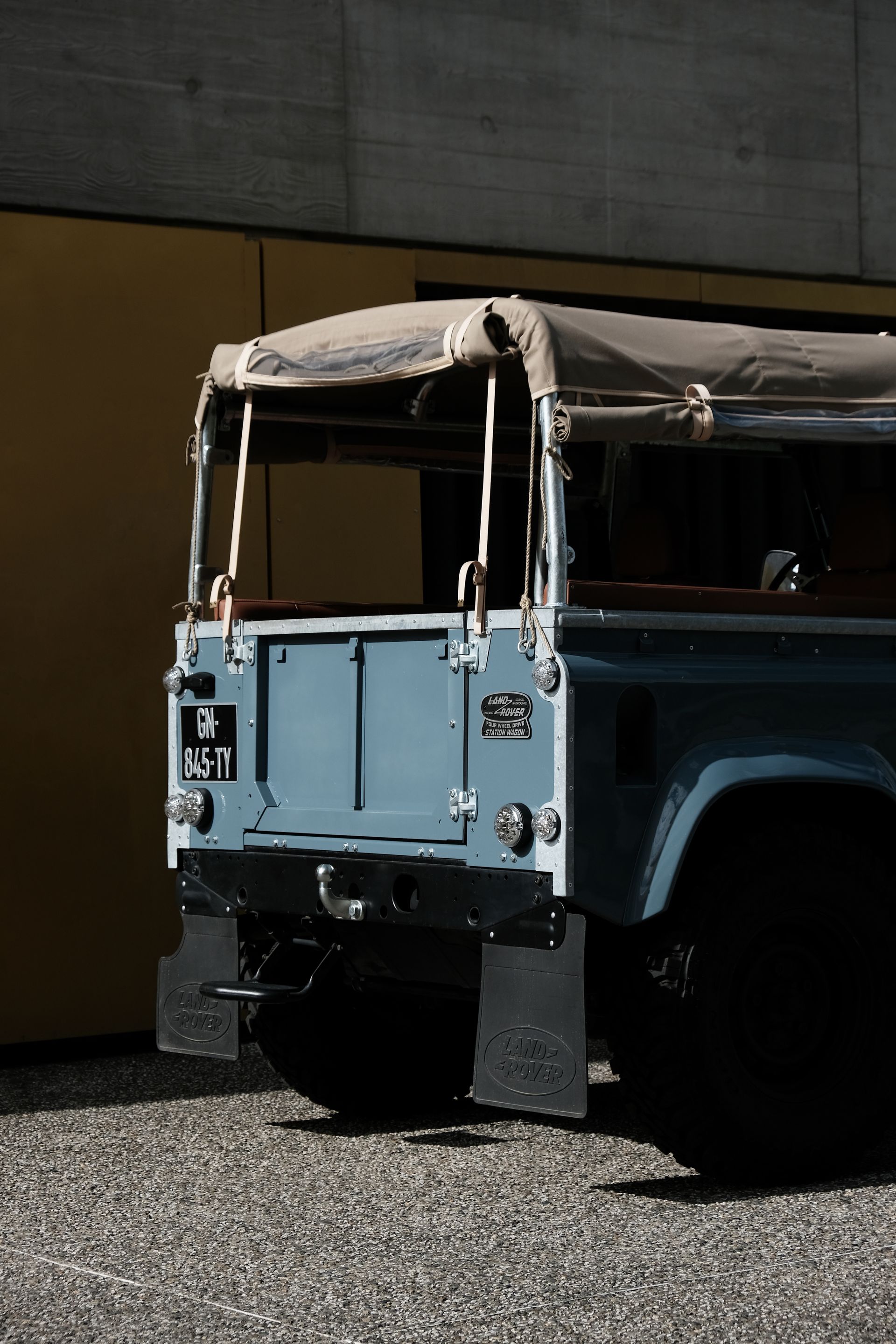 Land Rover bleu avec un toit en toile garé à l'extérieur d'un bâtiment jaune.
