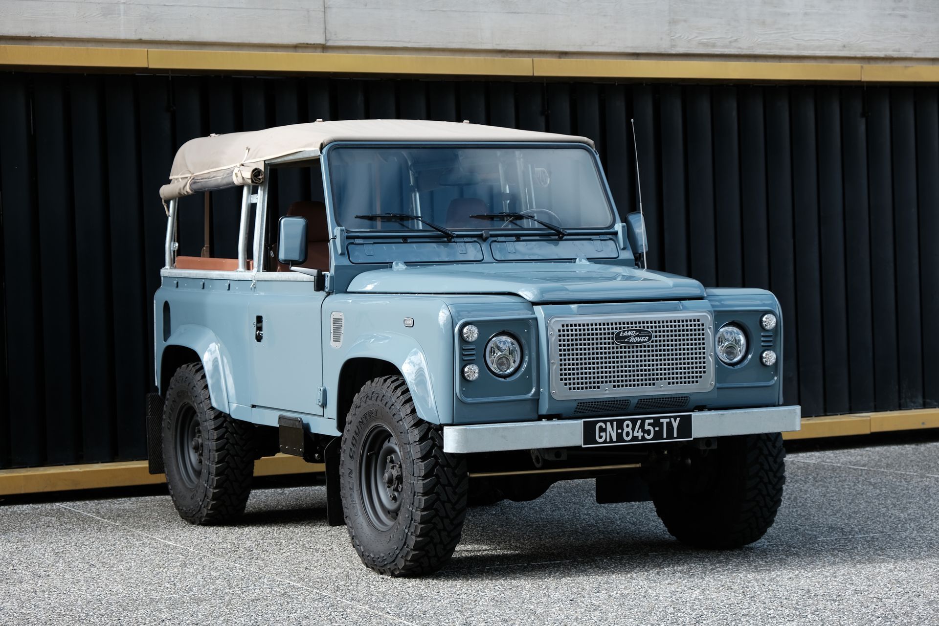 Land Rover Defender bleu clair avec un toit blanc garé devant un bâtiment sombre.