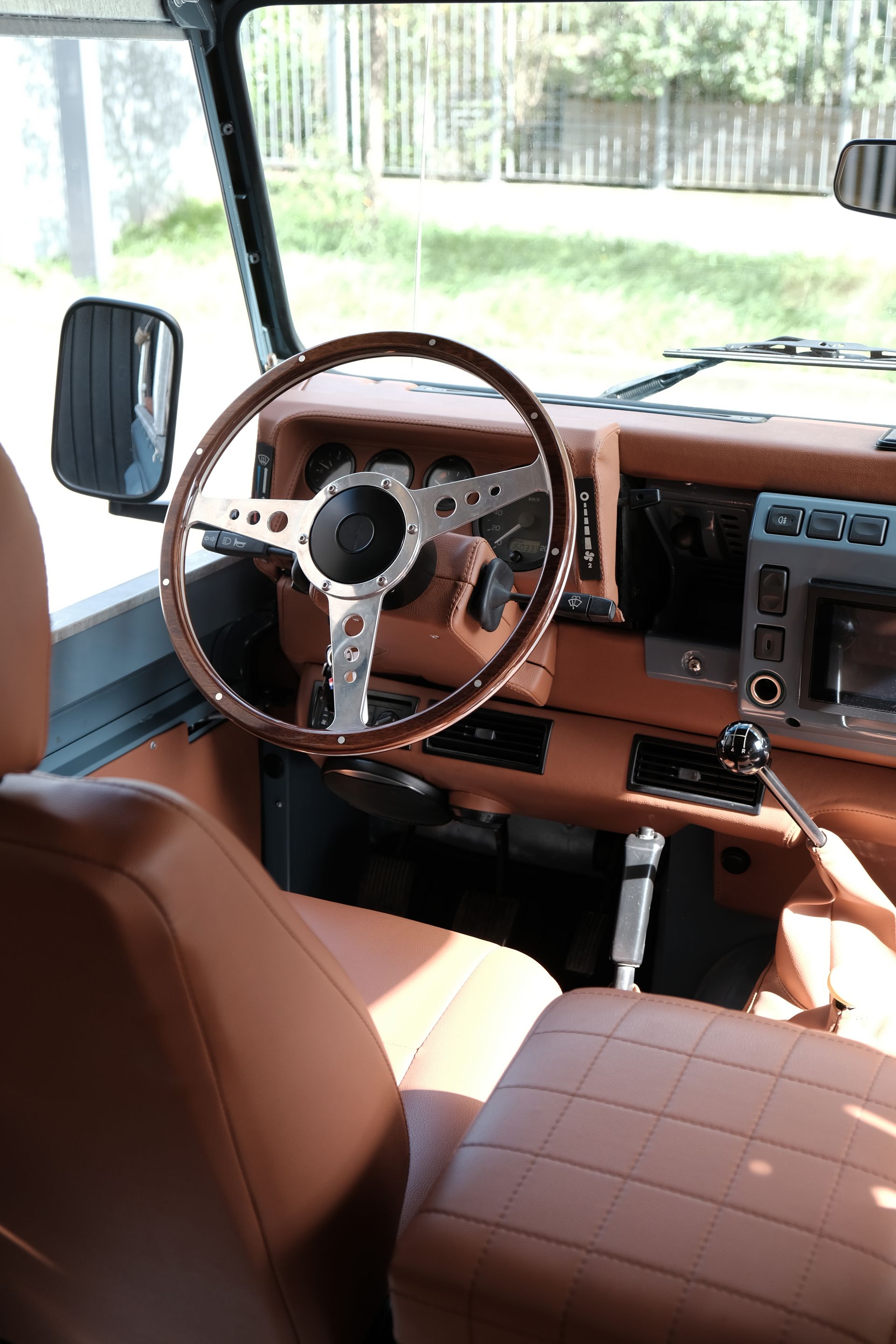 Vue intérieure d'un Land Rover Defender avec des sièges en cuir beige, un volant en bois et un tableau de bord moderne.