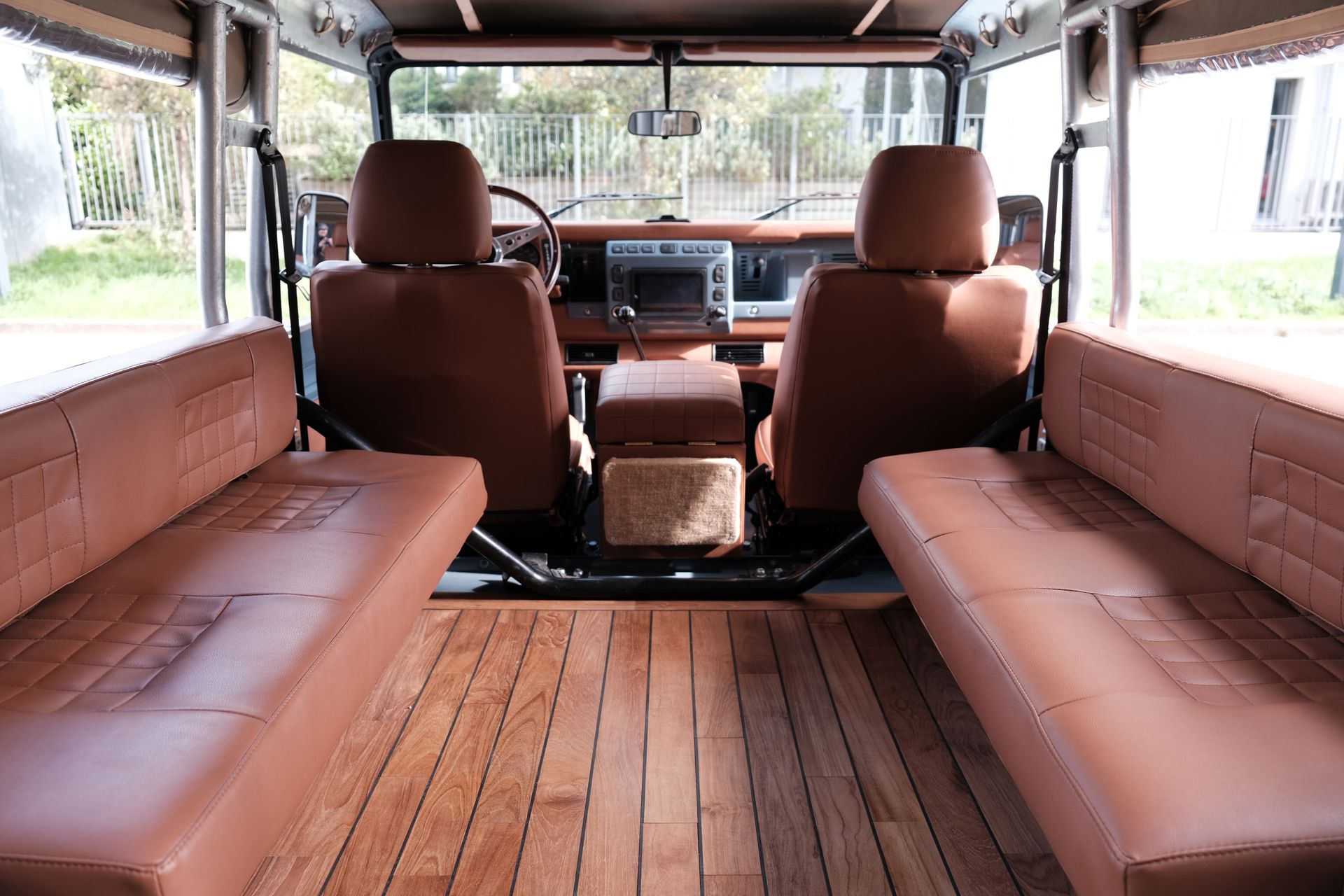 Intérieur d'un véhicule personnalisé marron avec sièges baquets avant, banquettes arrière et parquet teck.