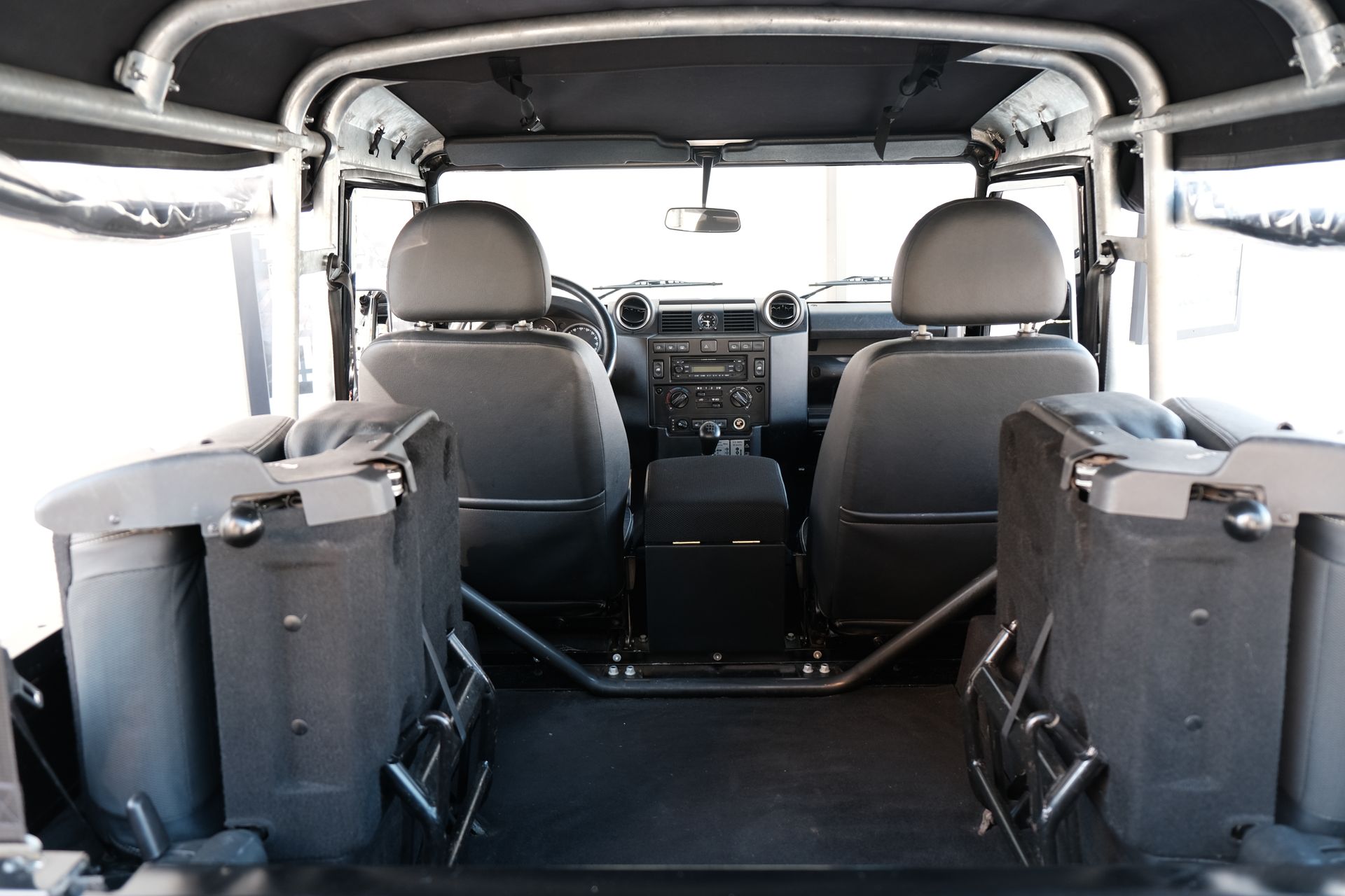Vue intérieure d'un Land Rover Defender noir, montrant les sièges avant, l'arceau de sécurité et les sièges arrière.