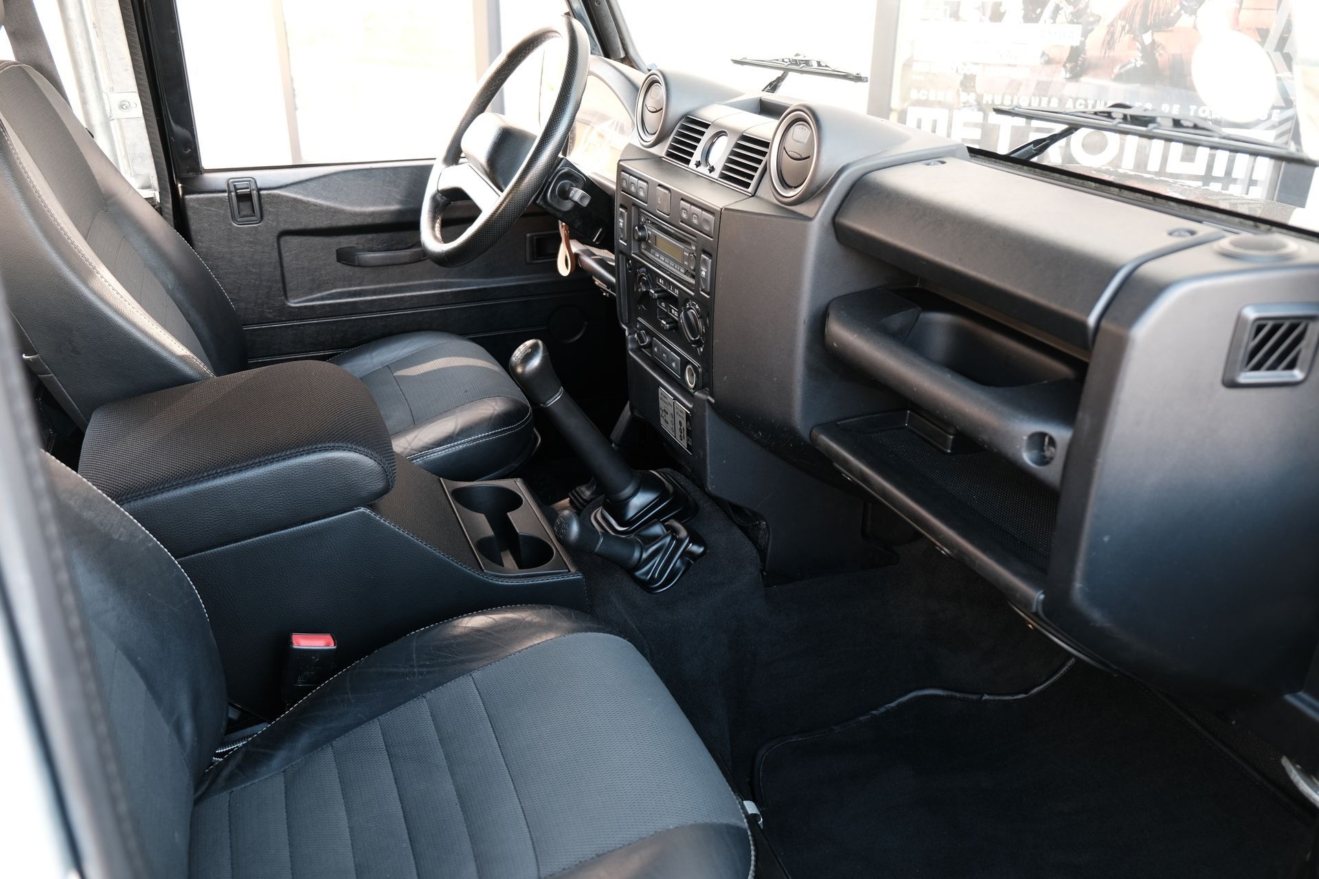 Intérieur d'un Land Rover Defender noir, montrant les sièges, le volant, le tableau de bord et le levier de vitesses.