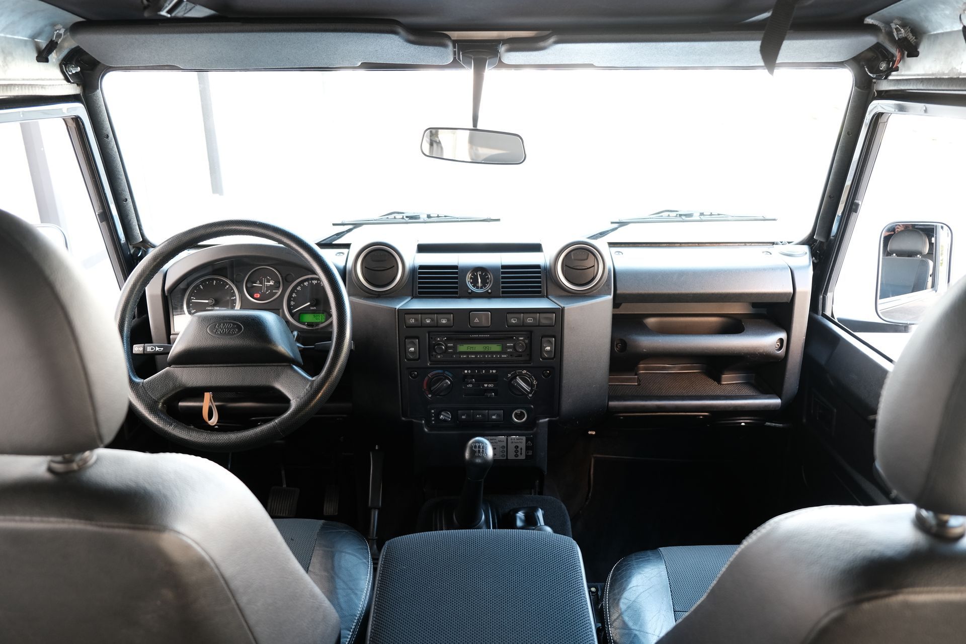 Intérieur d'un Land Rover Defender. Vue depuis les sièges arrière. Tableau de bord, volant et sièges noirs.