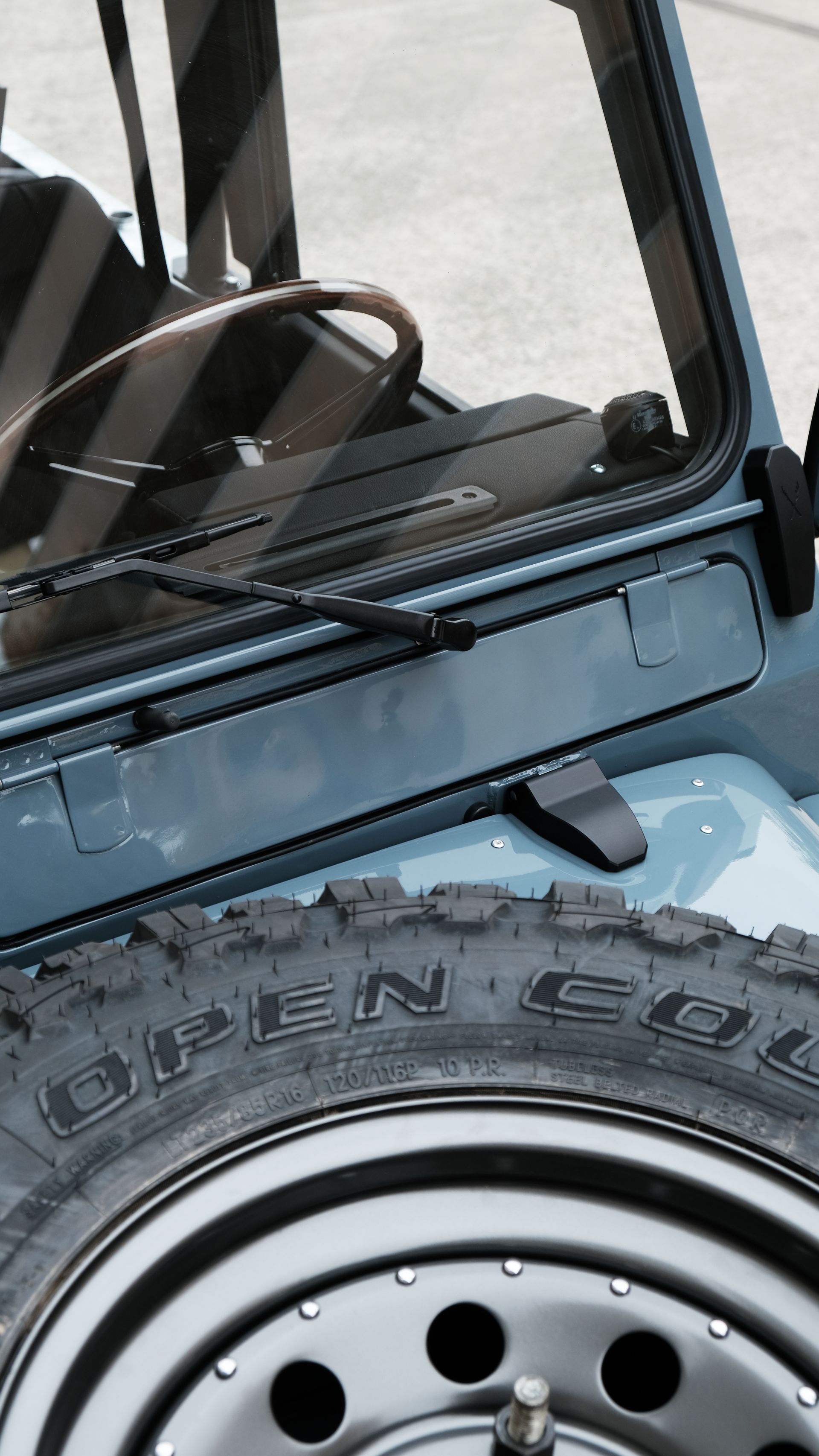 Gros plan de l'arrière d'un véhicule tout-terrain bleu, pneu de secours monté, roue noire et pare-brise avec essuie-glace.