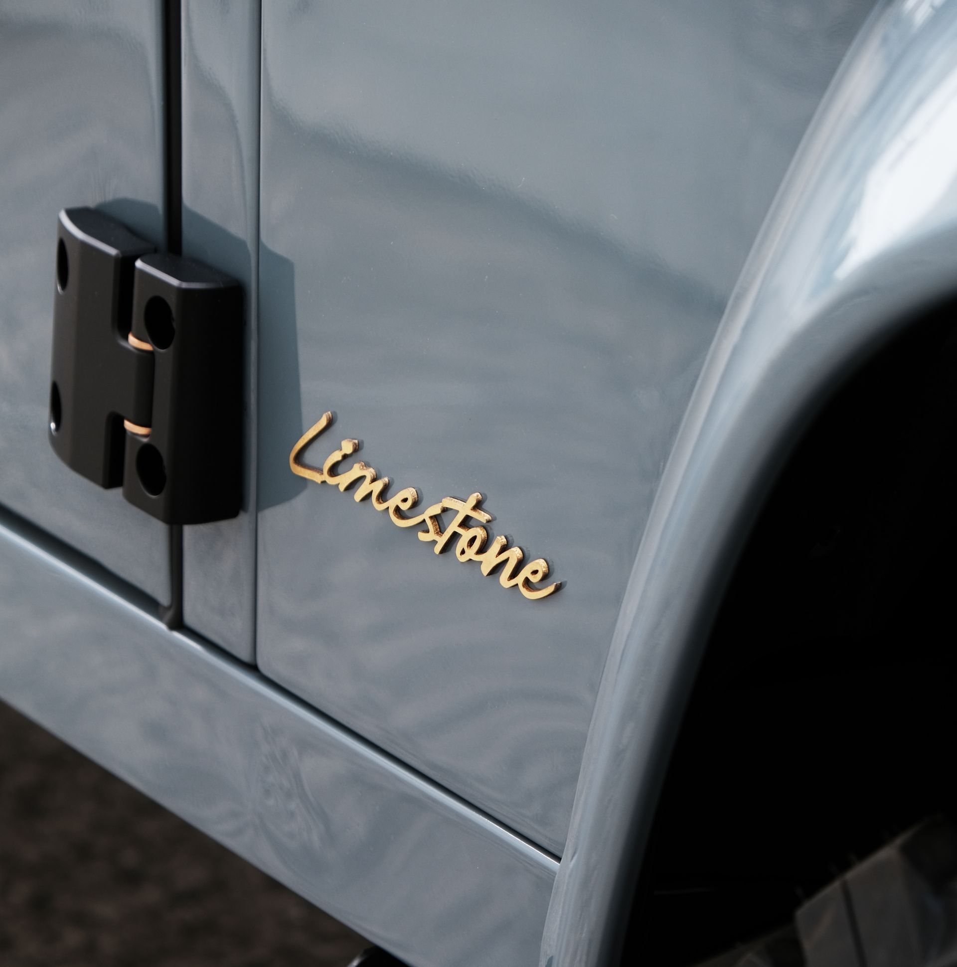 Gros plan d'une portière de voiture bleu clair, avec l'inscription « Limestone » dorée. Une charnière noire est visible.