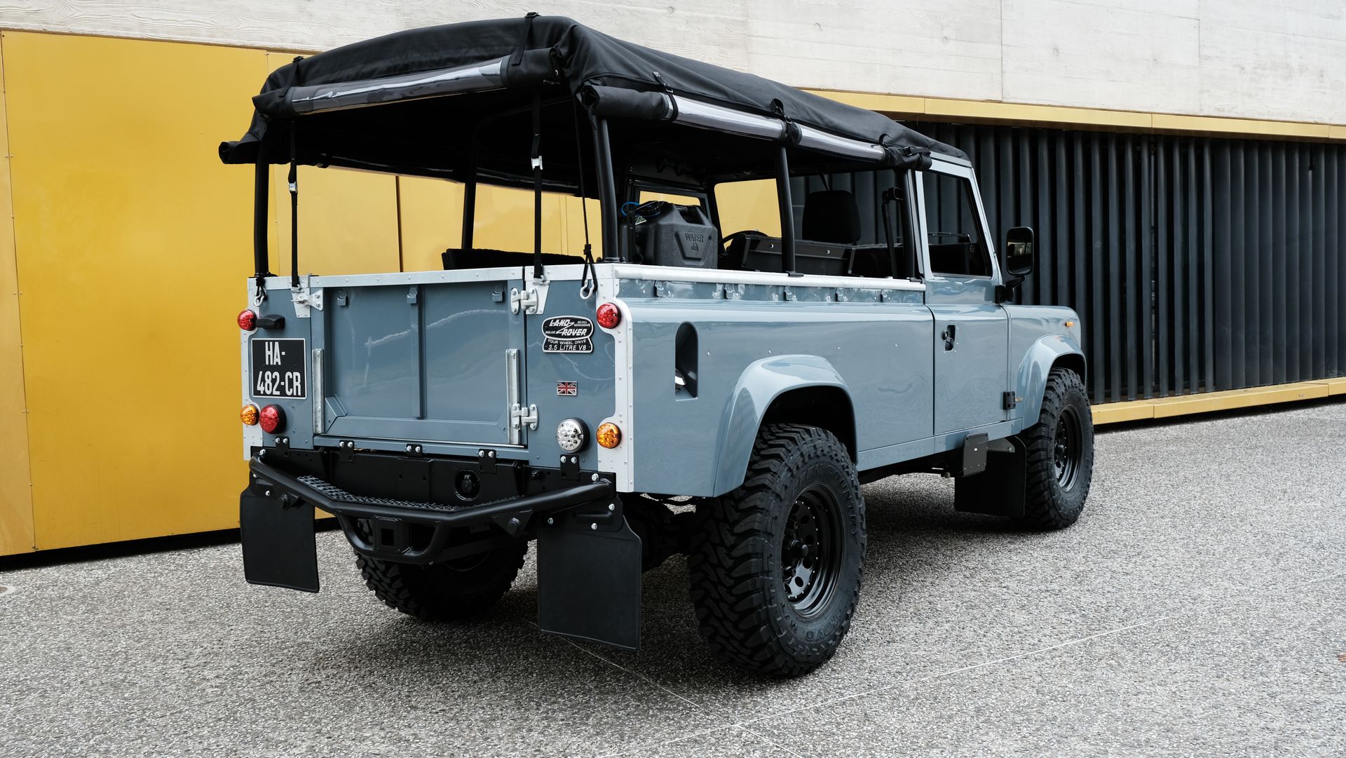 Land Rover Defender gris avec barres de toit noires, garé à l'extérieur.