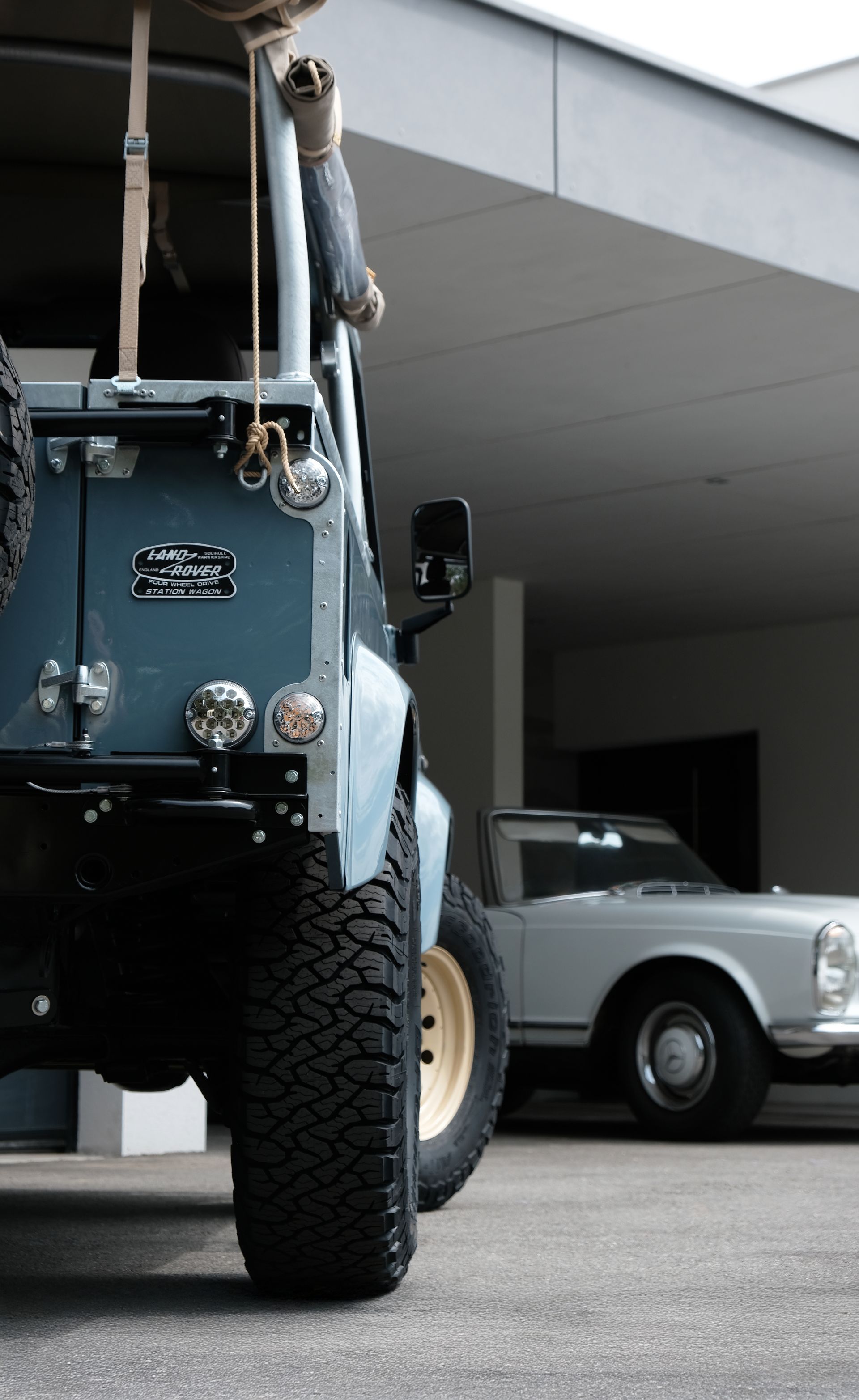 Véhicule tout-terrain bleu avec de gros pneus, garé près d'une voiture blanche vintage.
