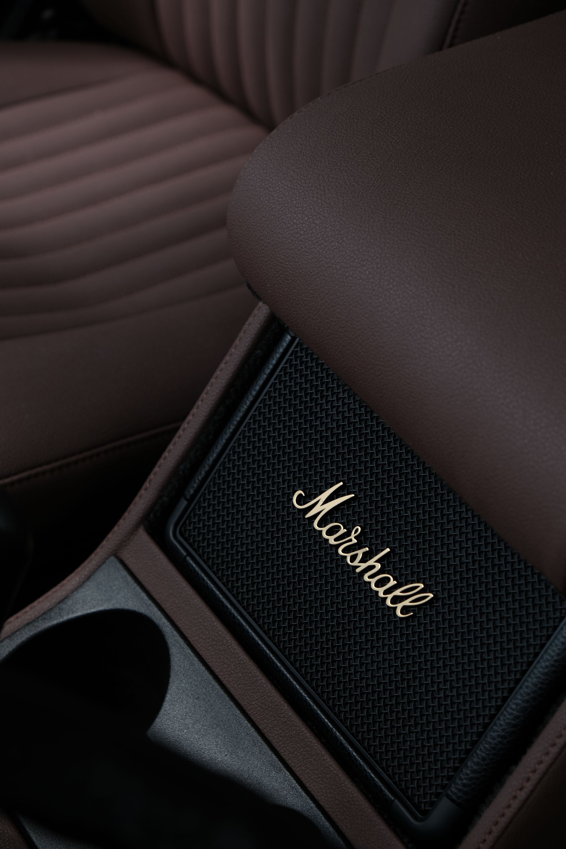 Gros plan de l'intérieur d'une voiture avec un haut-parleur Marshall intégré à la console, du cuir marron et des accents sombres.