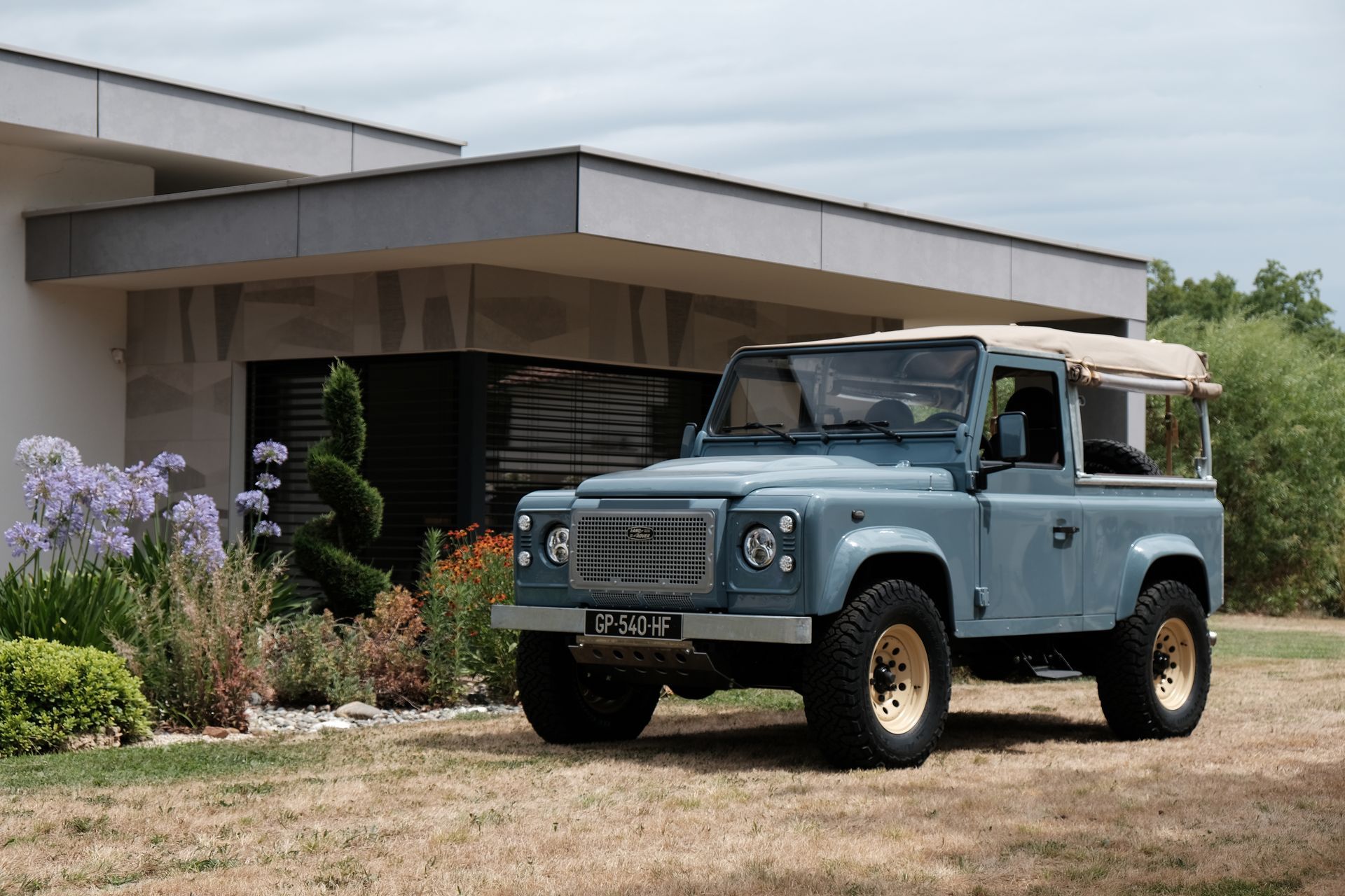 Land Rover Defender bleu garé devant un bâtiment moderne avec des roues beiges.