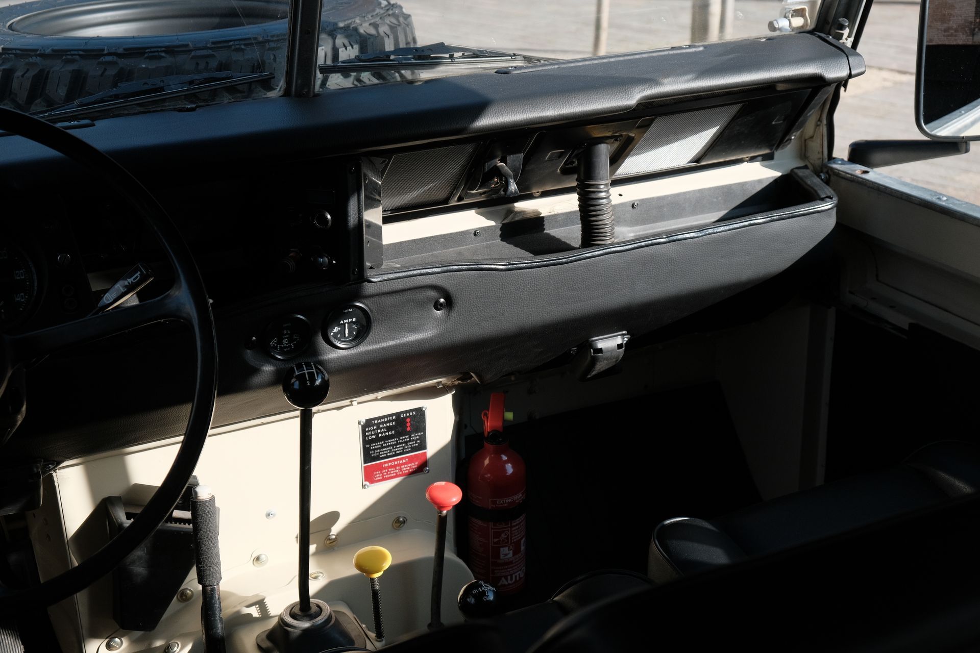 Vue intérieure d'un tableau de bord Land Rover vintage : couleurs noir et crème, leviers de vitesse, jauges et extincteur.