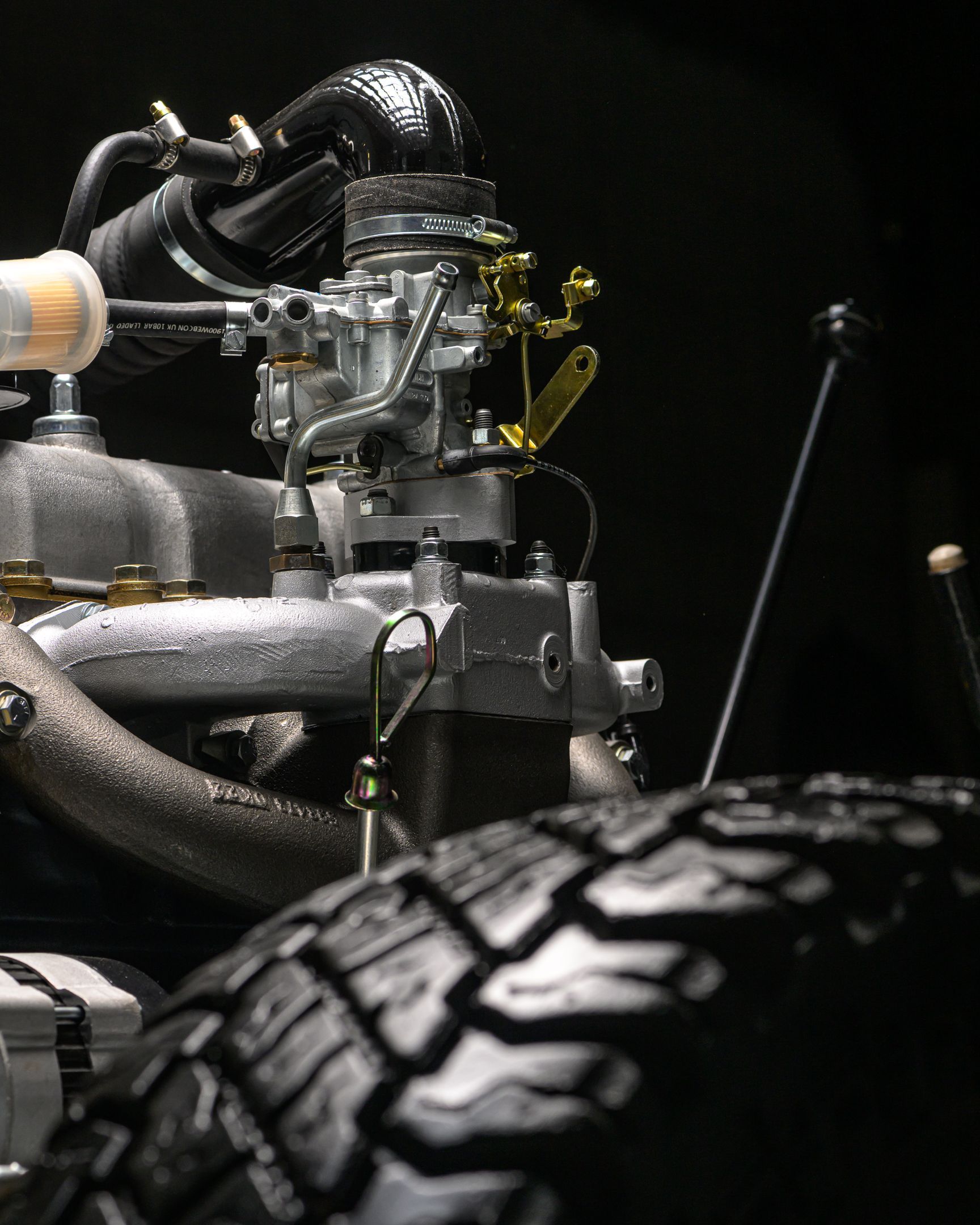 Gros plan d'un moteur détaillé, avec un accent sur le carburateur et la bande de roulement du pneu sur un fond sombre.