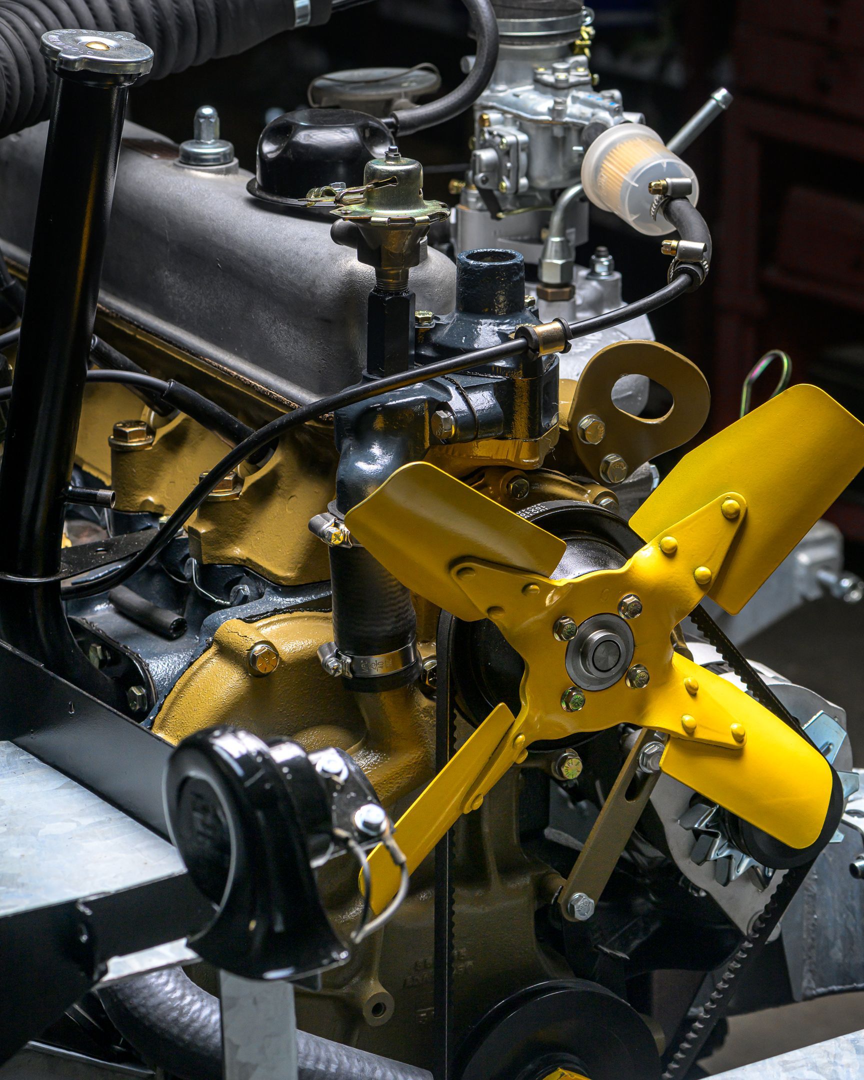 Ventilateur jaune et composants de moteur de voiture peints en or, avec carburateur visible et cadre noir.
