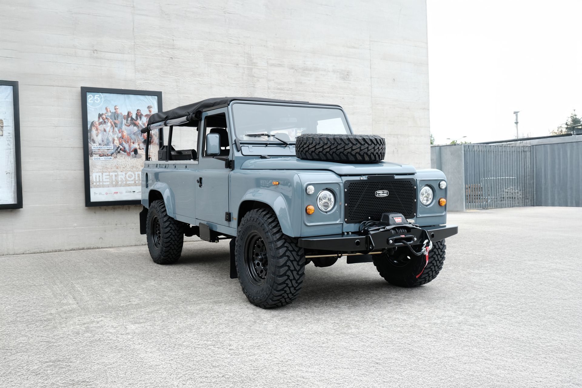 Land Rover Defender gris avec pneus noirs et toit garé à l'extérieur.